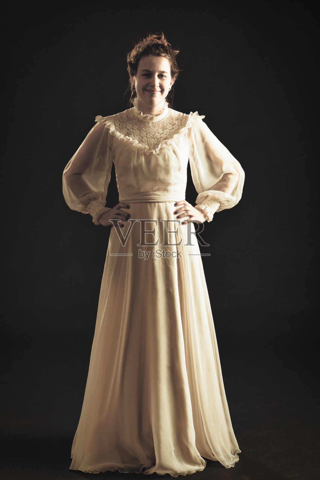 身着维多利亚蕾丝裙的年轻女子自信地站着，双手叉腰照片摄影图片