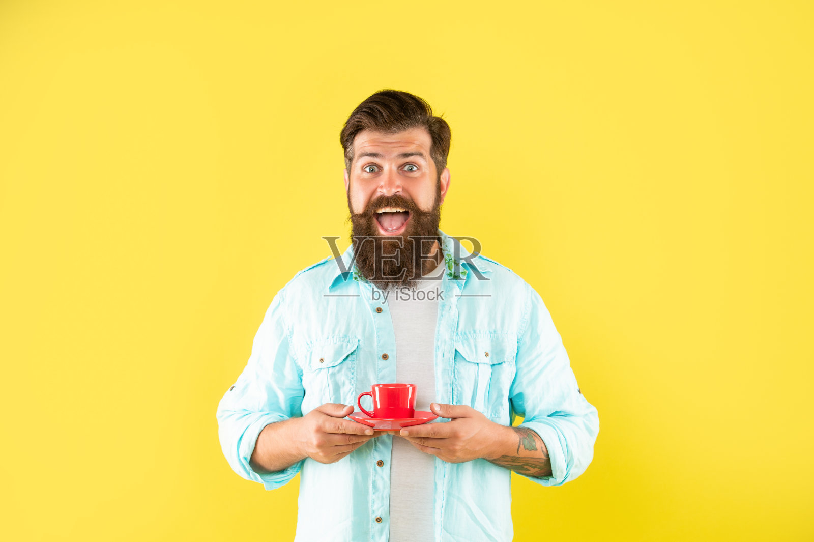 一名满脸胡须、兴高采烈的潮人手里拿着黄色背景的咖啡杯，早上好照片摄影图片