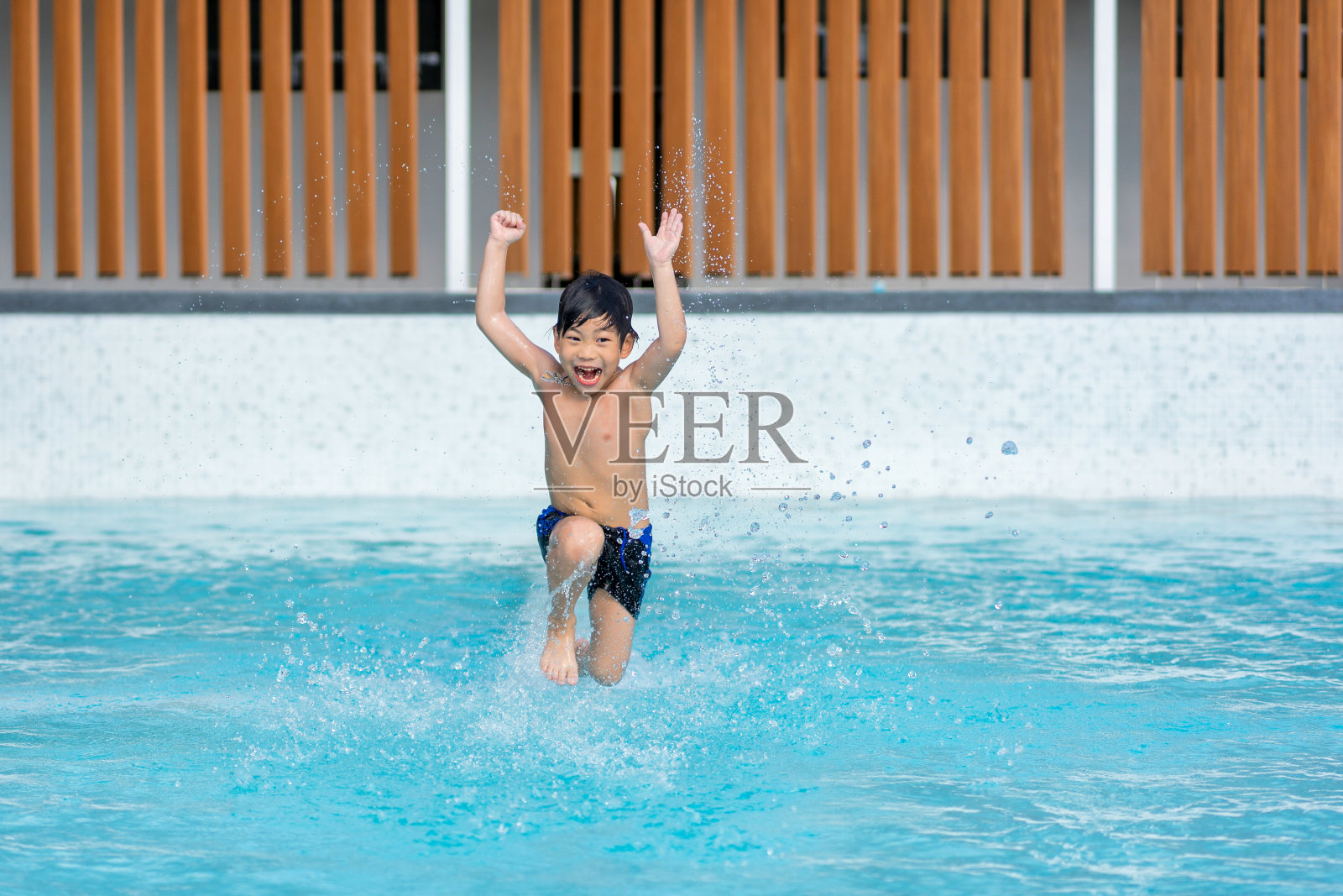 亚洲小男孩在游泳池里玩得很开心，他在夏天跳着玩水。照片摄影图片