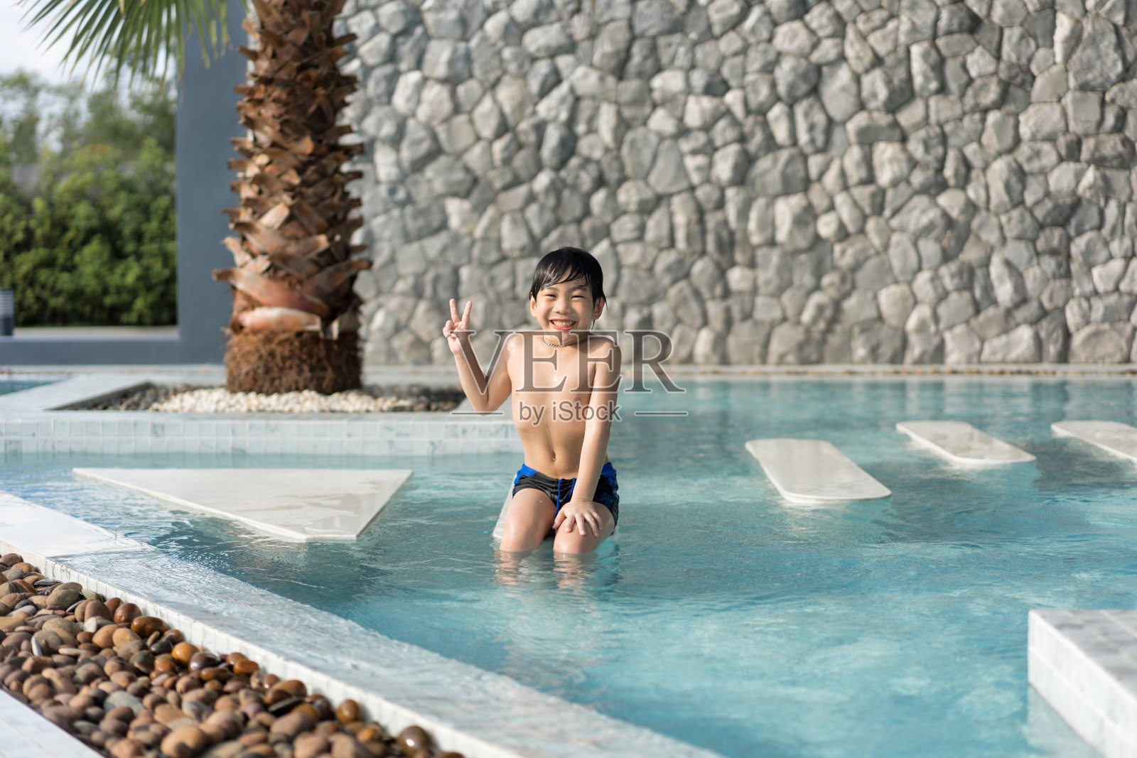 亚洲小男孩在游泳池里玩得很开心，他在夏天跳着玩水。照片摄影图片