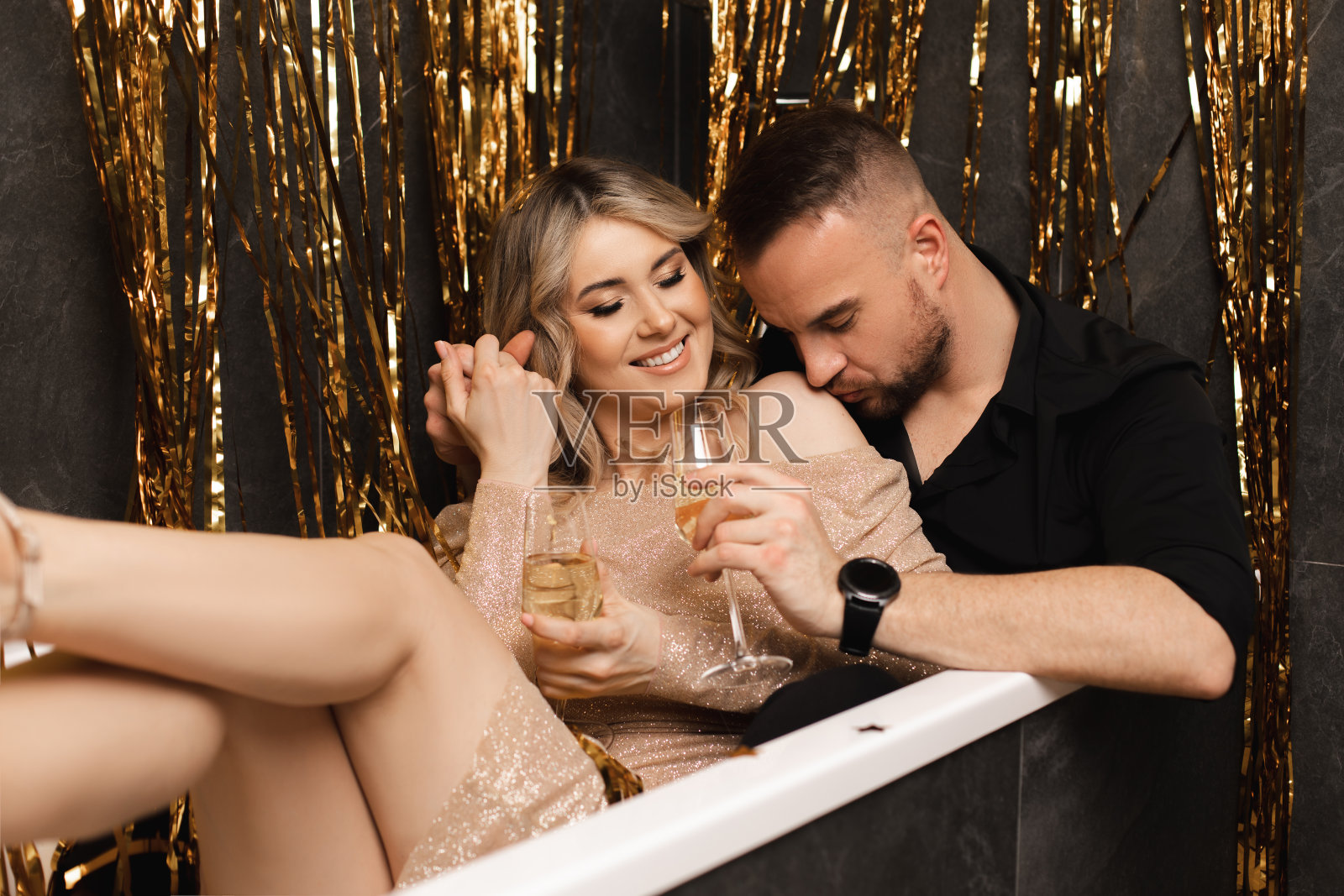 微笑和大笑的夫妇的肖像，女人和男人坐在浴缸喝香槟。庆祝乔迁庆宴照片摄影图片