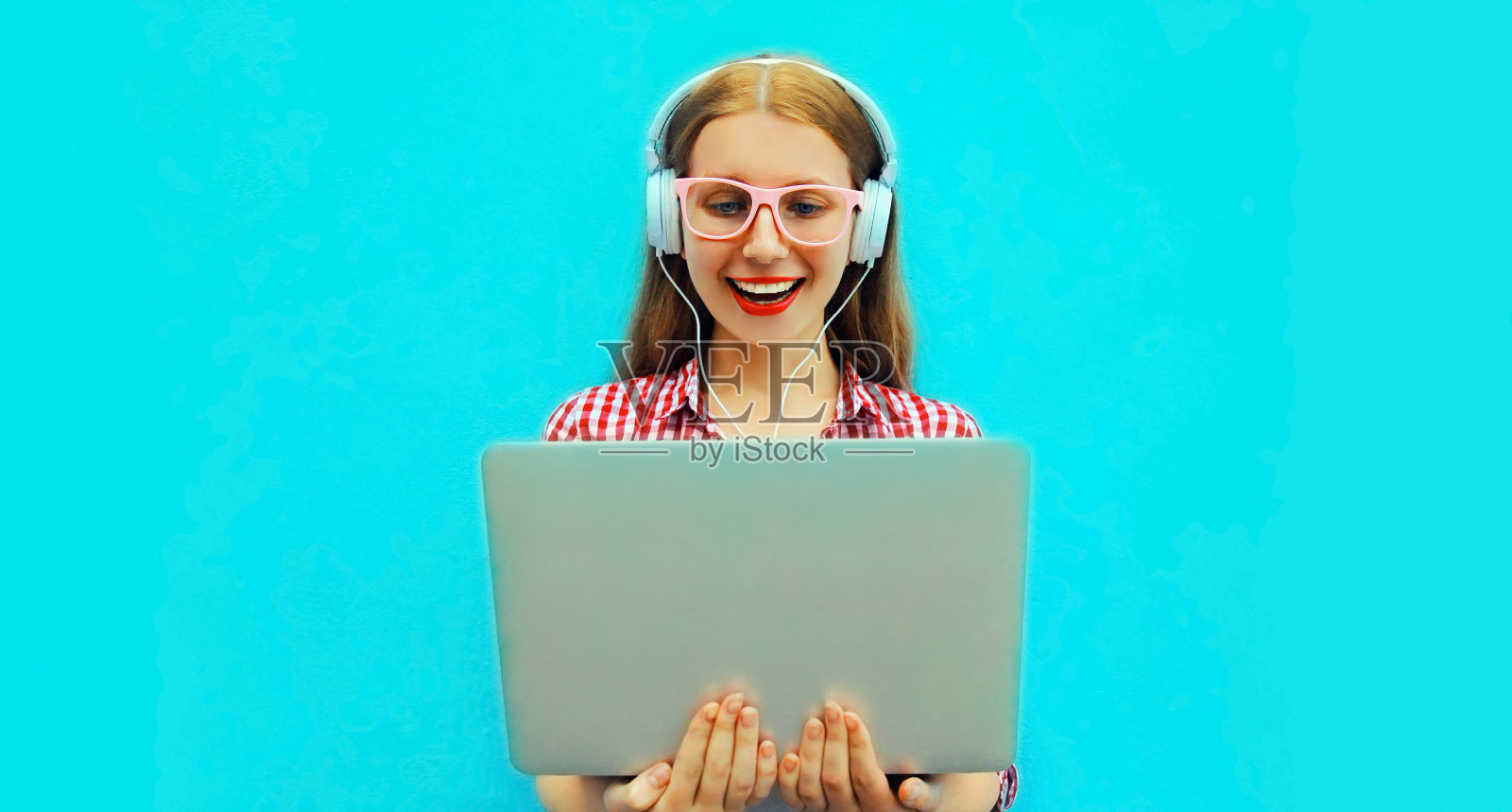 现代年轻女性的肖像与笔记本电脑听音乐在蓝色背景耳机照片摄影图片