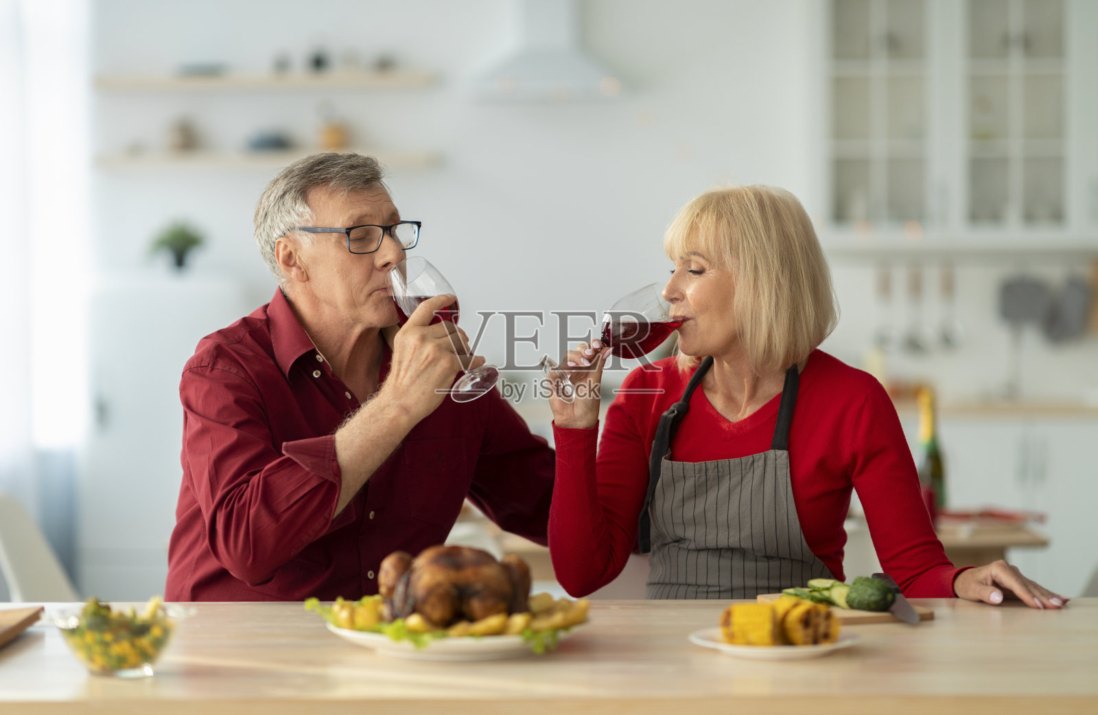 在厨房里，一对深情的老夫妇一边喝着红酒，一边准备圣诞大餐，烤火鸡照片摄影图片