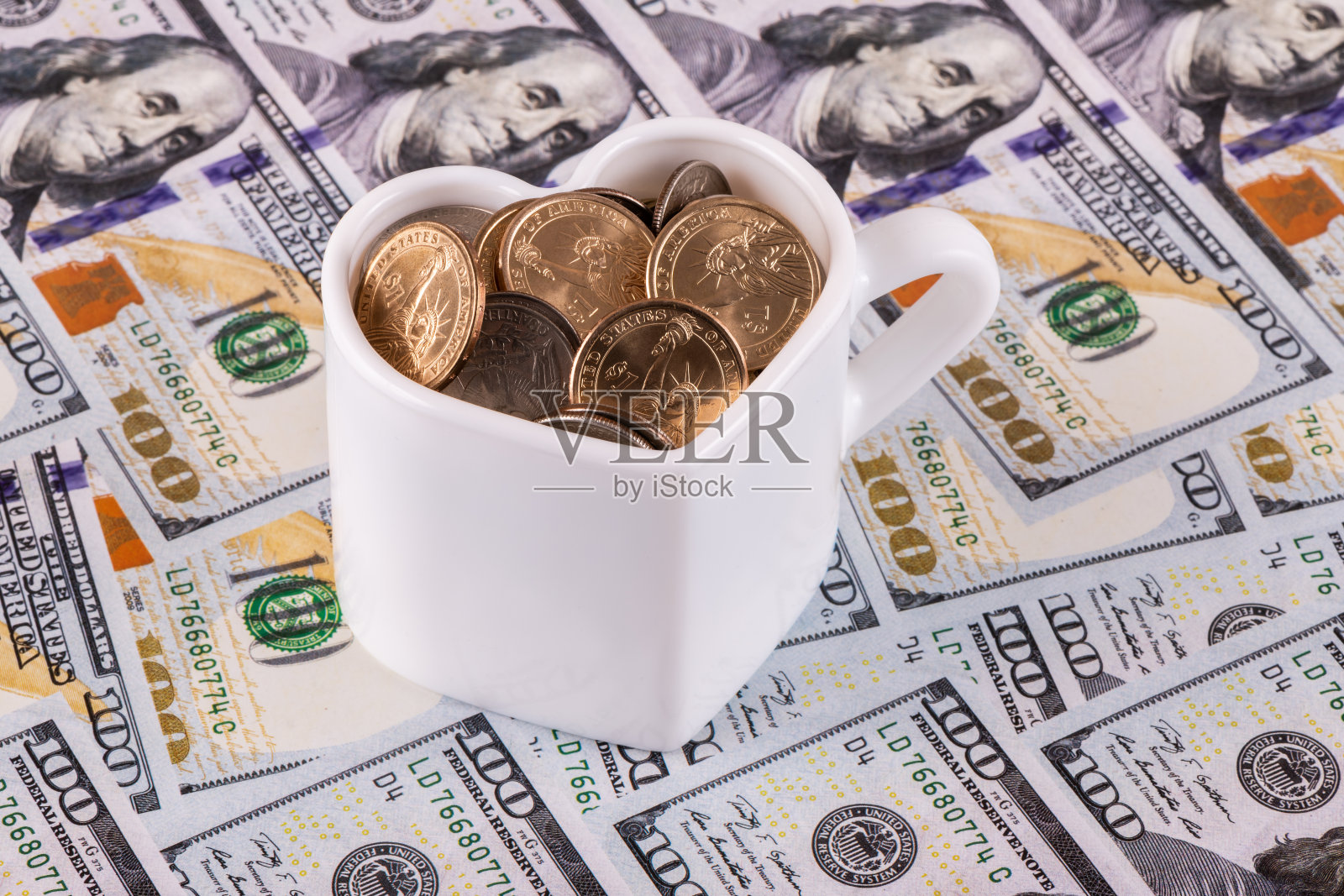 一个装满美国硬币的杯子，背景是100美元钞票照片摄影图片