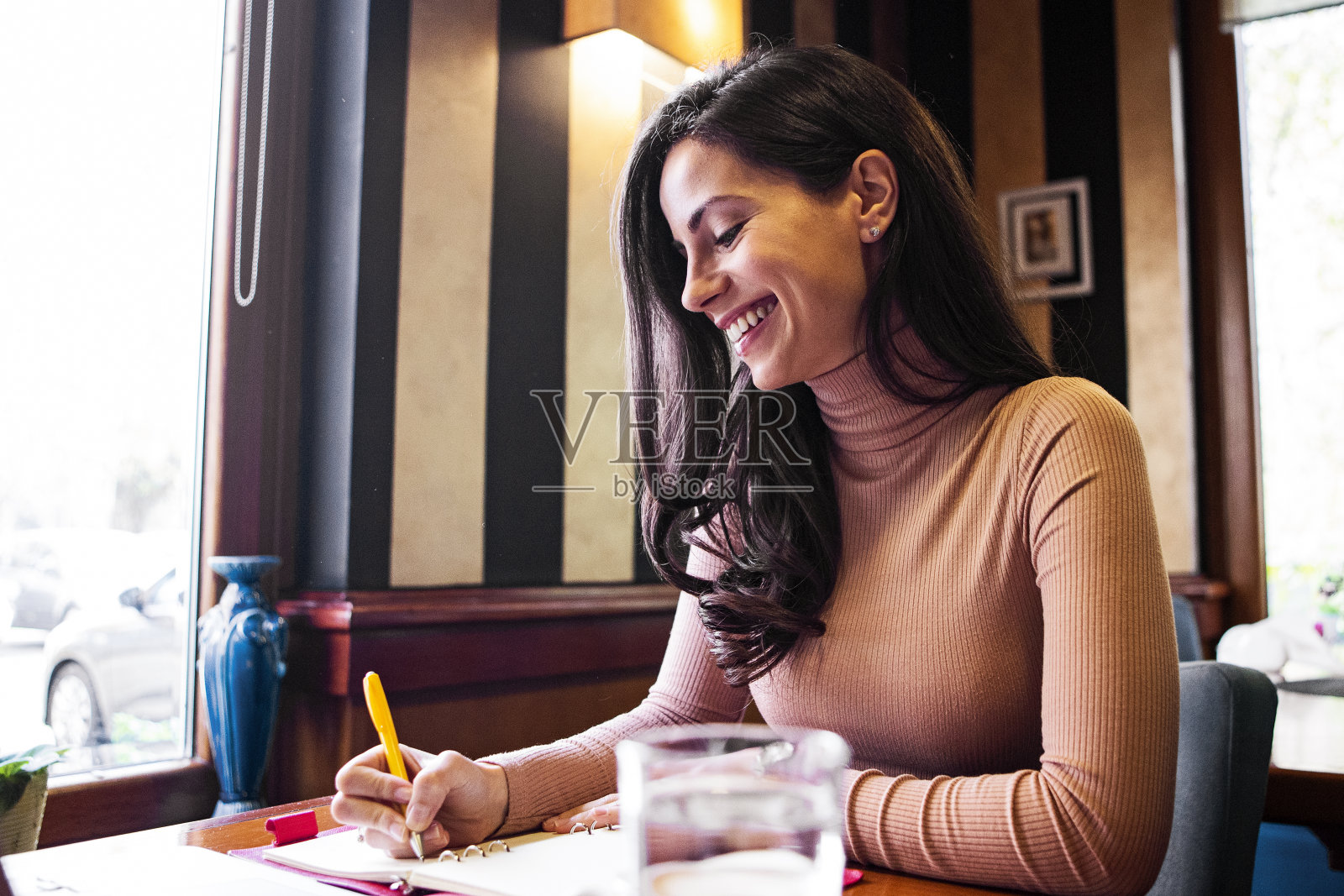 一个微笑的年轻女子坐在咖啡馆里写作照片摄影图片