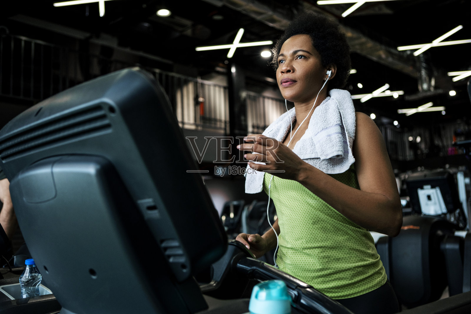 非裔美国妇女在健身房跑步机上跑步，脖子上围着毛巾照片摄影图片