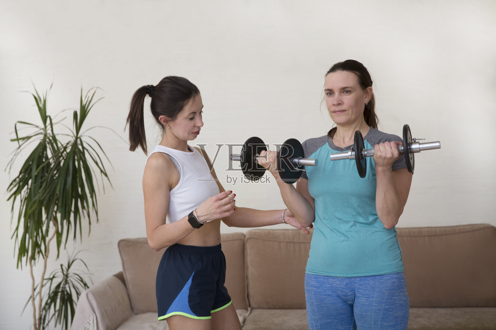 健康女性在私人教练的指导下在家里用哑铃锻炼身体。照片摄影图片