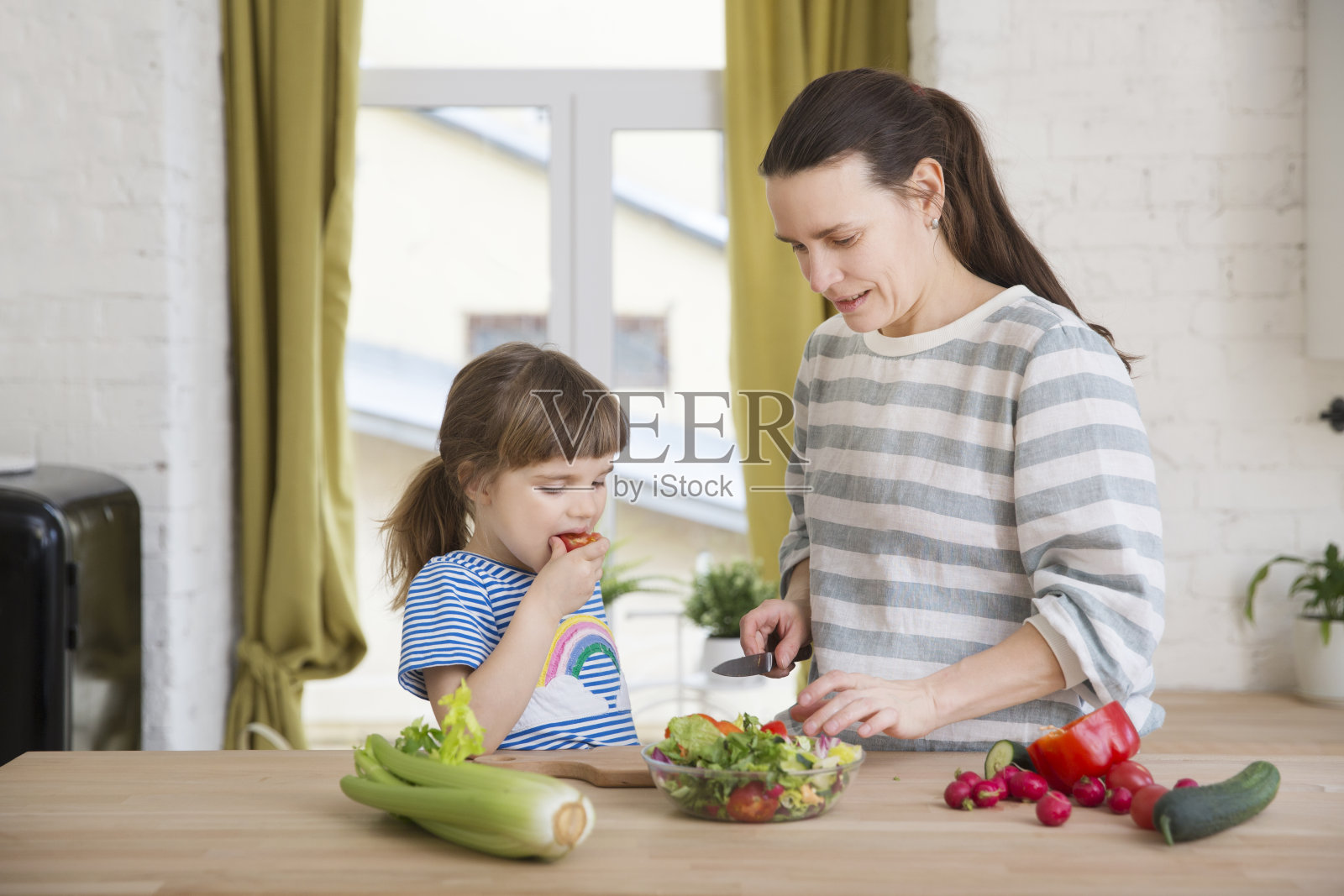 妈妈和小女儿在家里的厨房里一起做沙拉。健康的饮食习惯照片摄影图片