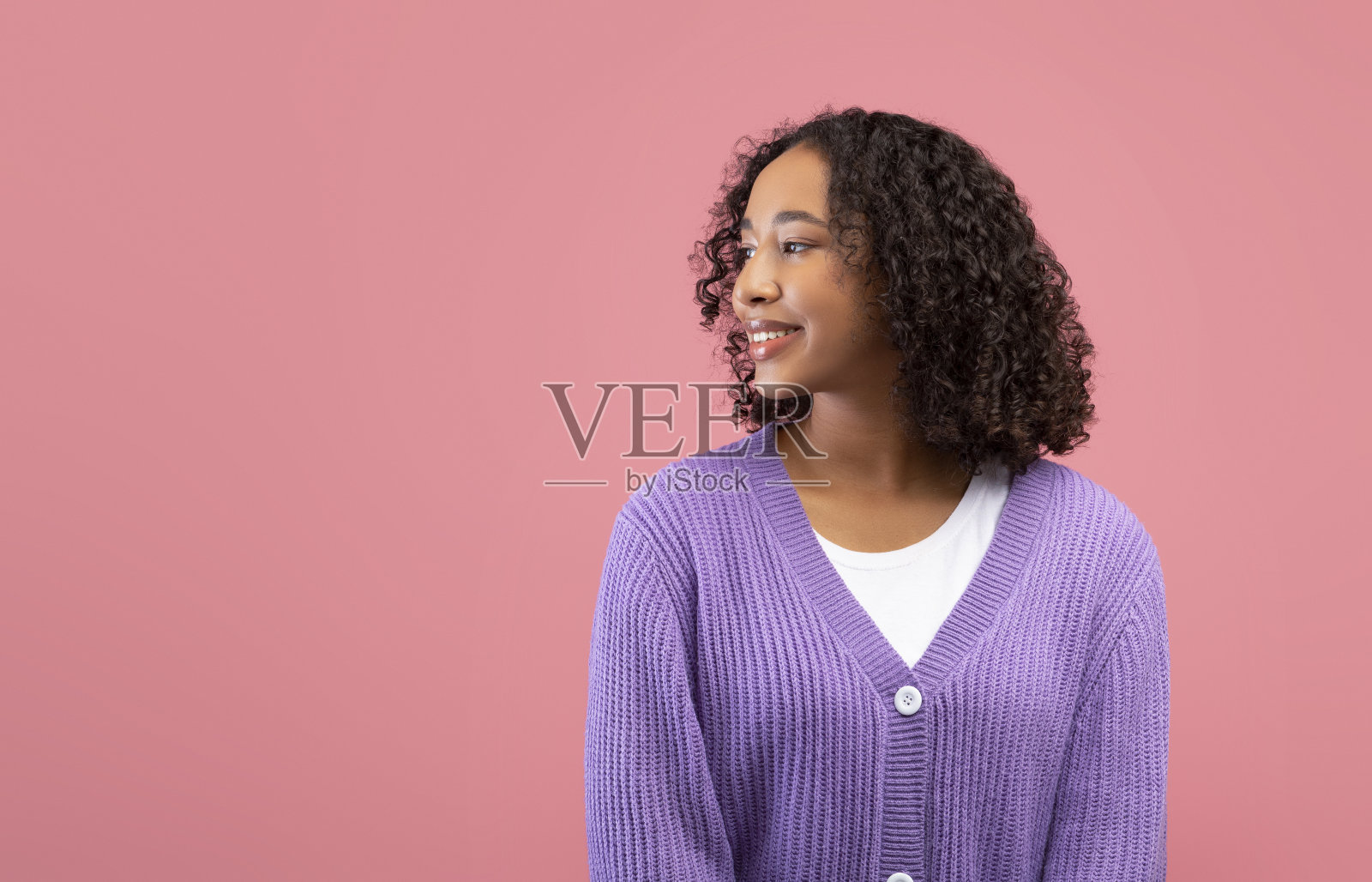 漂亮年轻的黑人女士在休闲穿着微笑，看着一边的空白空间在粉红色的工作室背景照片摄影图片