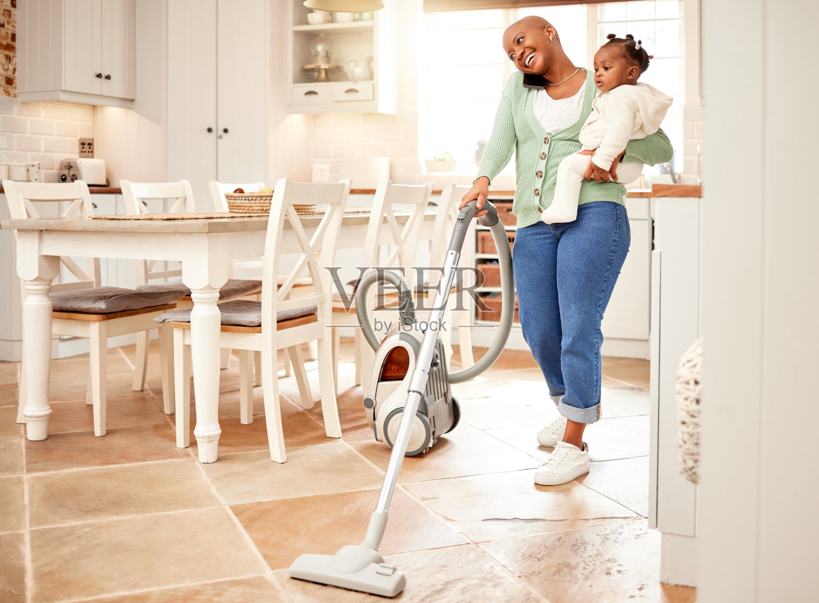 一个有吸引力的年轻女人的全长镜头吸尘和打电话，同时携带她的女儿在家里照片摄影图片