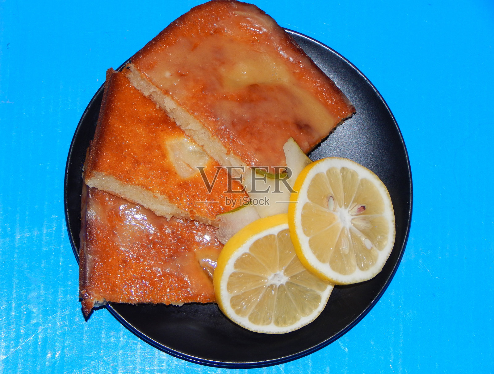 配梨和柠檬片的蛋糕。蓝色背景上的沙漠照片摄影图片