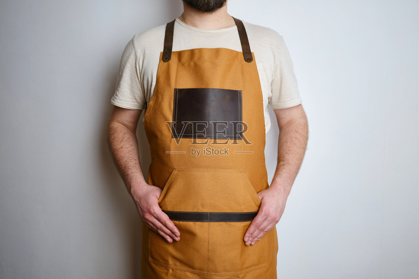 一个穿着厨房围裙的男人。厨师负责烹饪。穿着制服和防护服做饭。食品服务的工作。专业烹饪。驼色面料围裙，休闲时尚服装。英俊的贝克摆姿势照片摄影图片