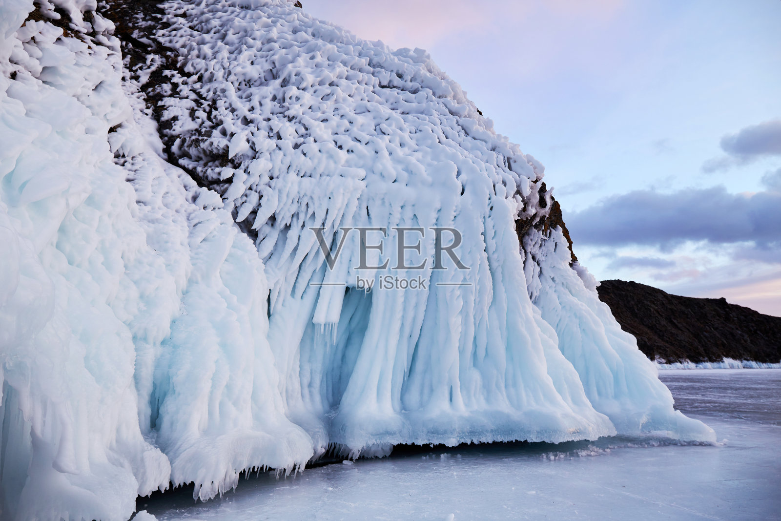 岩石上覆盖着雪和冰柱。日落时冰冻的贝加尔湖照片摄影图片