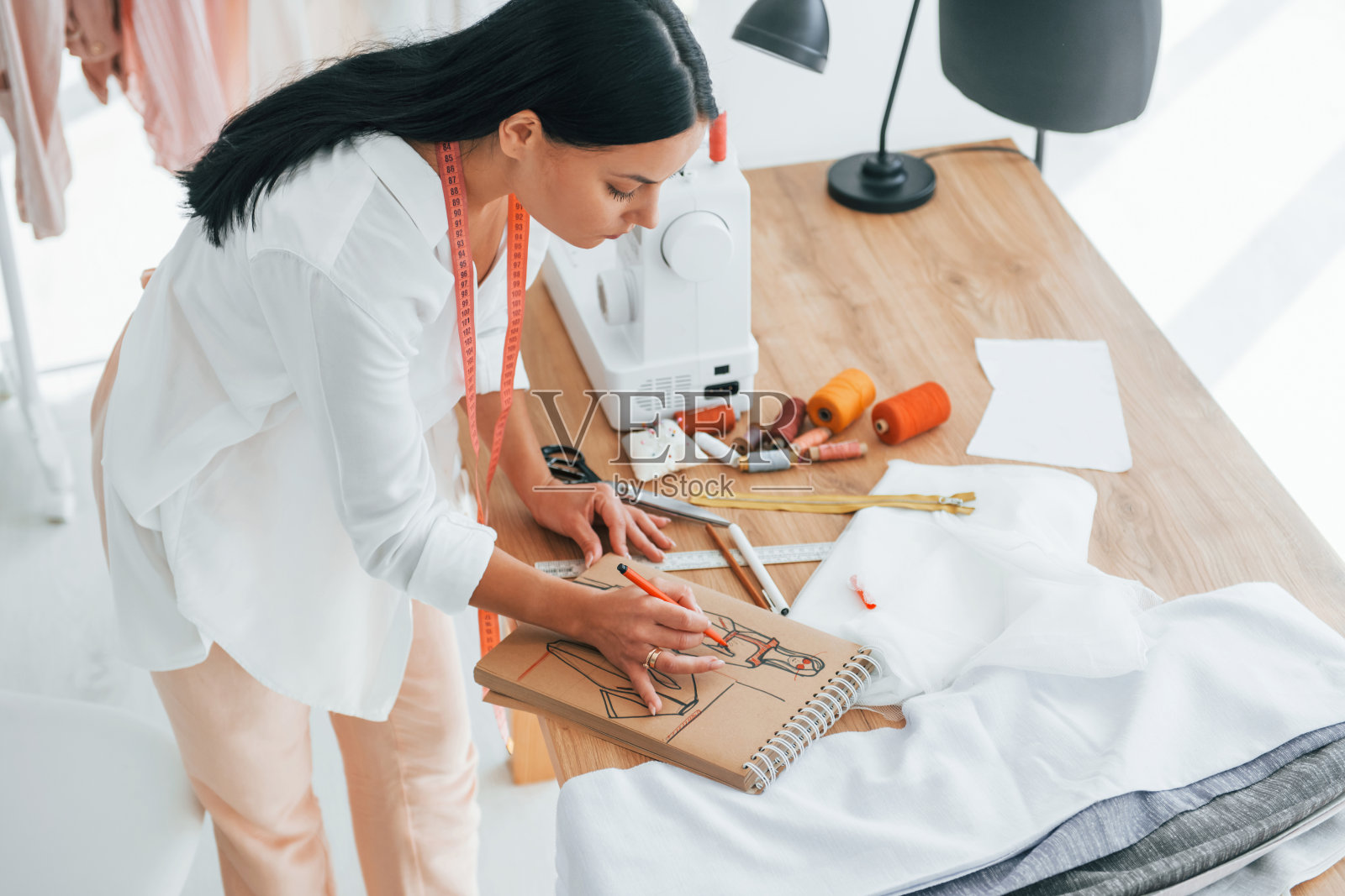 忙于工作。女裁缝在她的办公室里穿着不同的衣服照片摄影图片