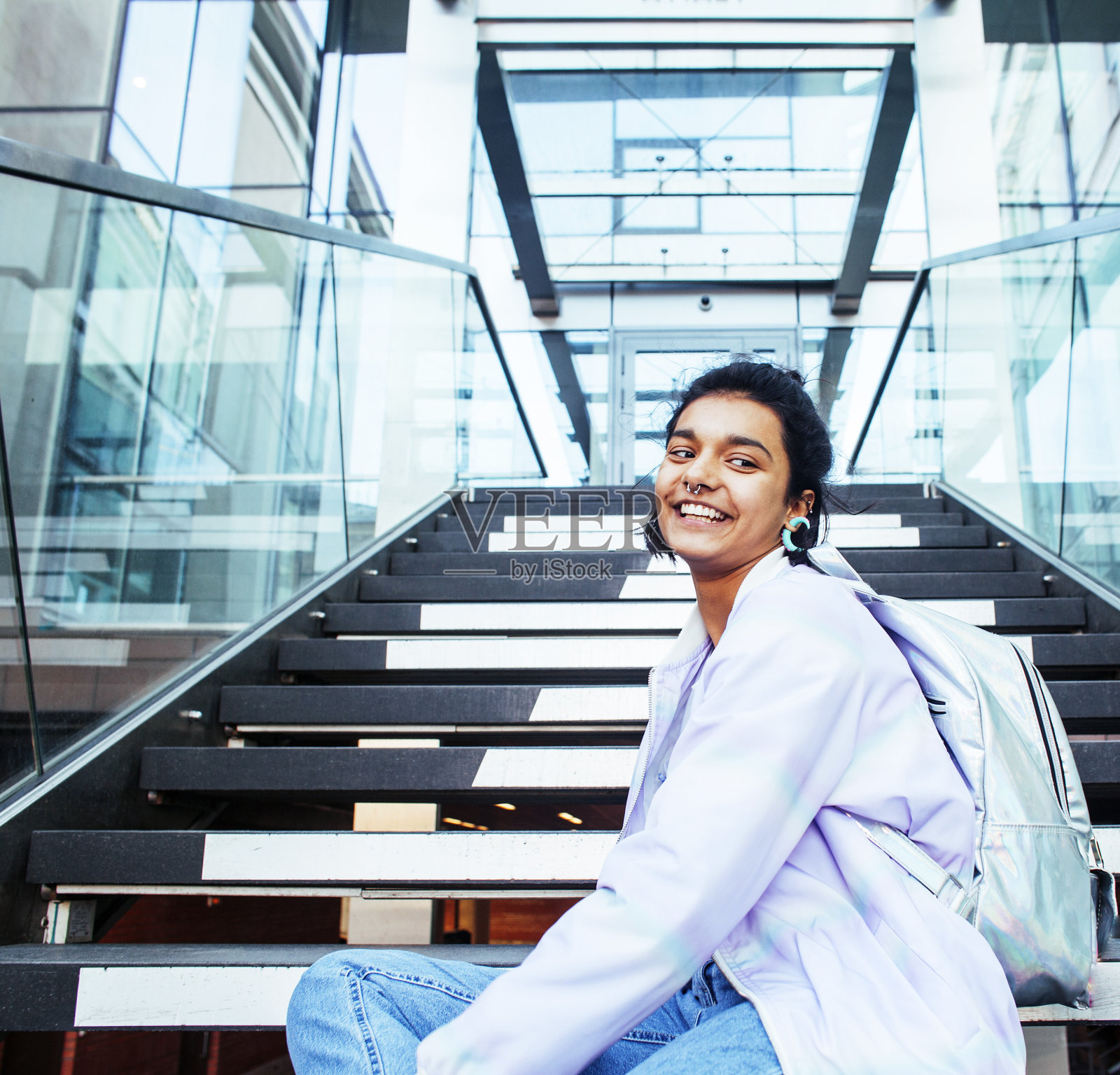 年轻可爱的印度女孩在大学大楼的楼梯上看书，戴着时髦的眼镜，生活方式的人的概念近距离照片摄影图片