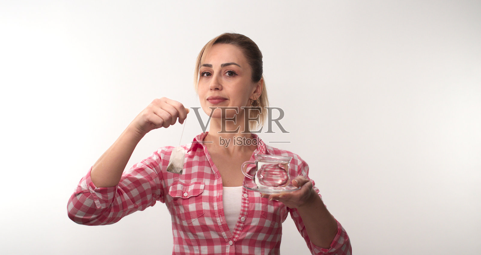 年轻幸福的女人站在白色的背景上，手里拿着热腾腾的红茶袋。照片摄影图片