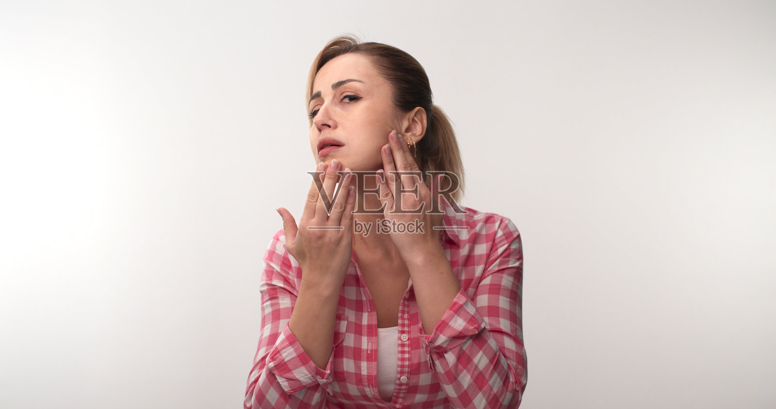 年轻女子在白色背景下检查自己的皮肤。照片摄影图片