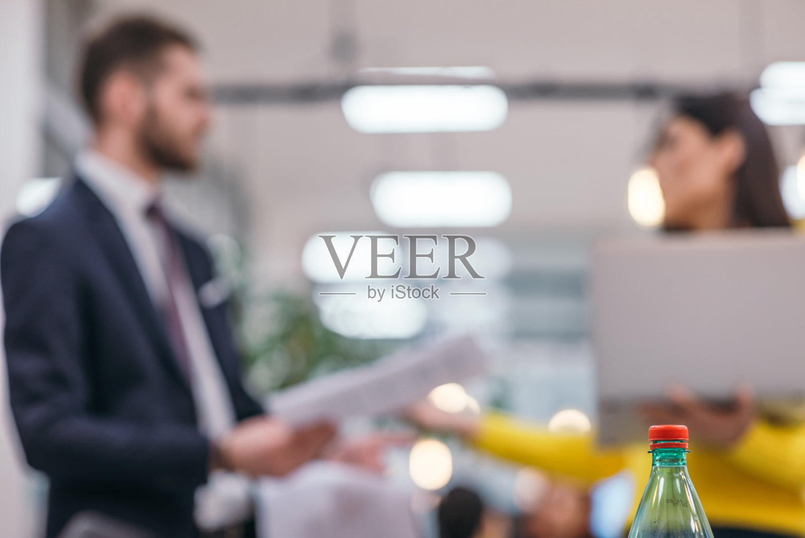 这是一张模糊的照片，一位商人老板站在一间现代化的初创公司办公室里，检查他的女雇员交给他的文件。照片摄影图片