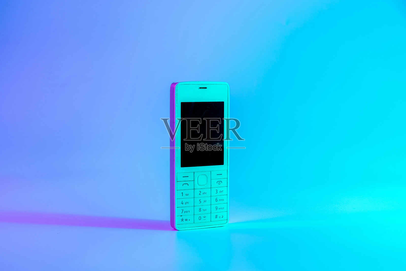 复古手机的概念。白色的旧手机在霓虹灯下，粉红色的蓝光。复古的波。波普艺术。最小的思想概念。照片摄影图片