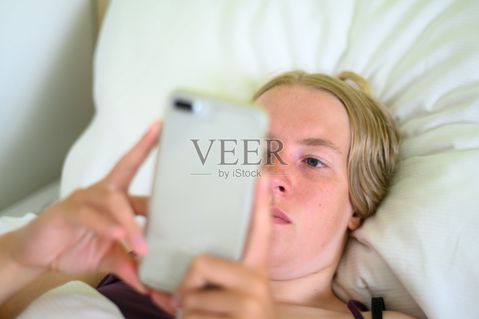 一位金发女性使用智能手机，躺在床上休息照片摄影图片