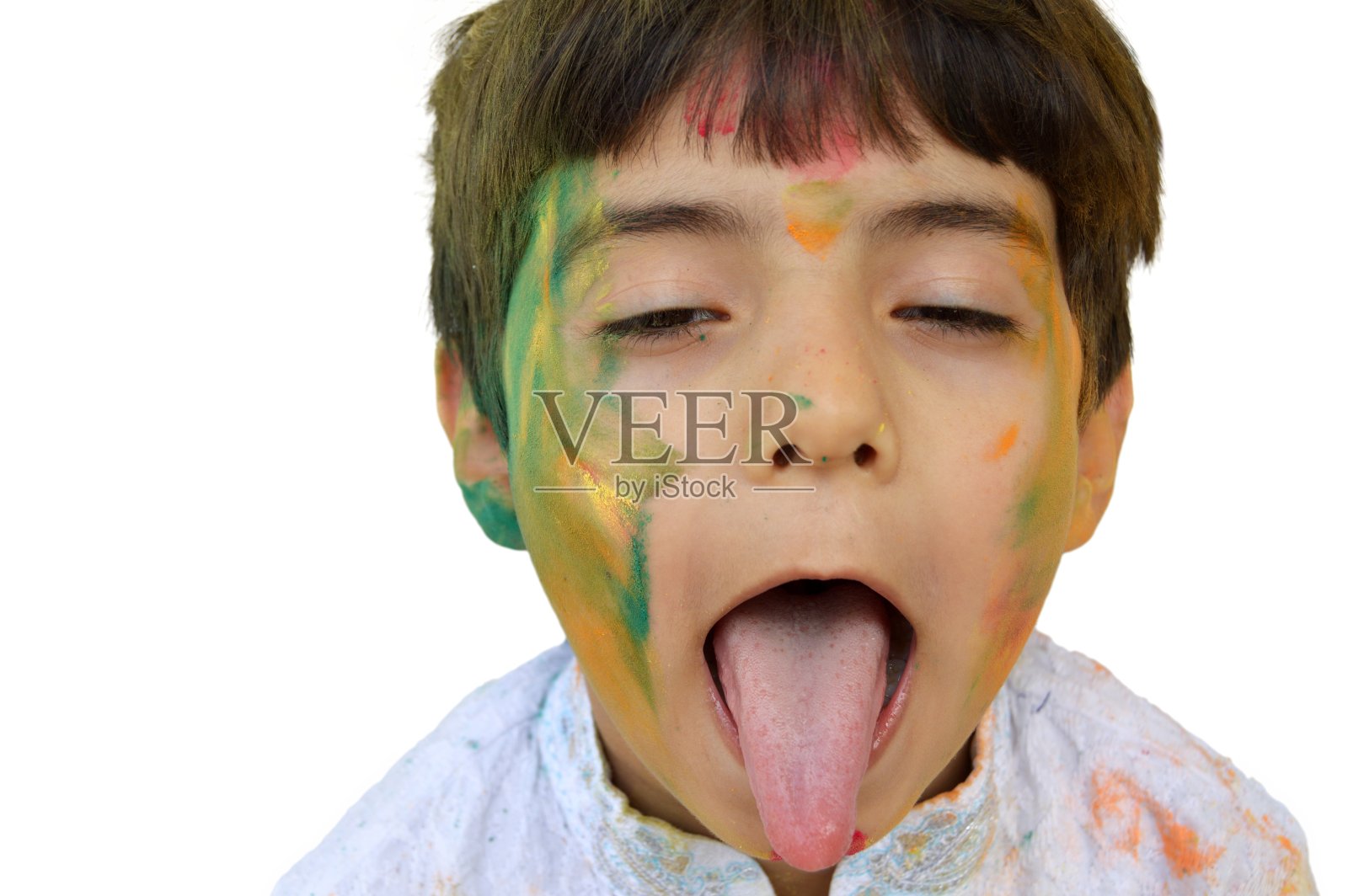 有趣的小男孩穿着白色的库尔塔，露出他的舌头，脸和头发涂着胡里节粉彩，孤立在白色之上照片摄影图片