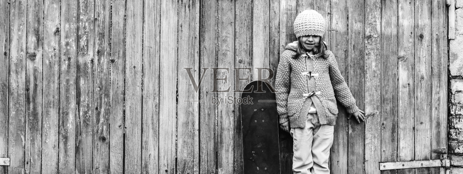 水平横幅或头部与可爱的小女孩在冬季羊毛衣服与滑板，而站在垃圾木制背景-活动和好玩的童年-复制空间的概念照片摄影图片