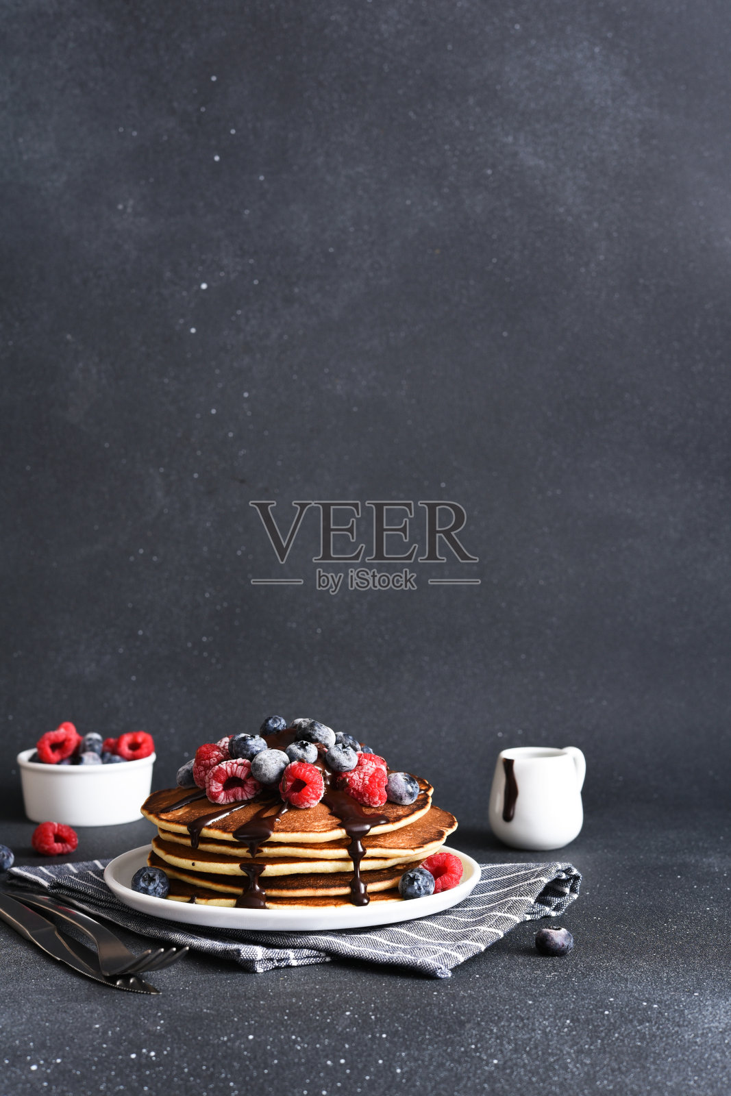 煎饼配上覆盆子，蓝莓和巧克力酱，背景是深色混凝土。一堆煎饼和浆果照片摄影图片