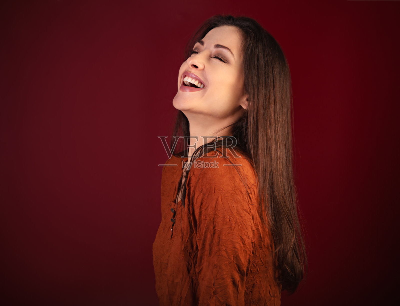 美丽的快乐微笑的女人在暗红色的背景与空的复制空间。特写侧面观肖像的自然女性情感。照片摄影图片