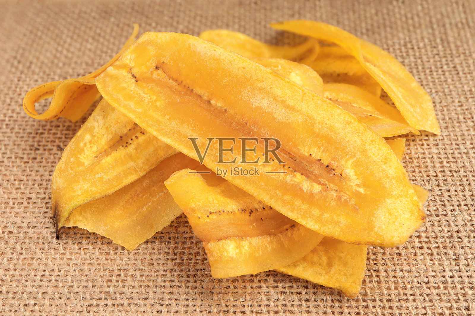一堆酥脆的香蕉片薯片，油炸或烤香蕉片在粗麻袋纹理背景与选择性焦点。照片摄影图片
