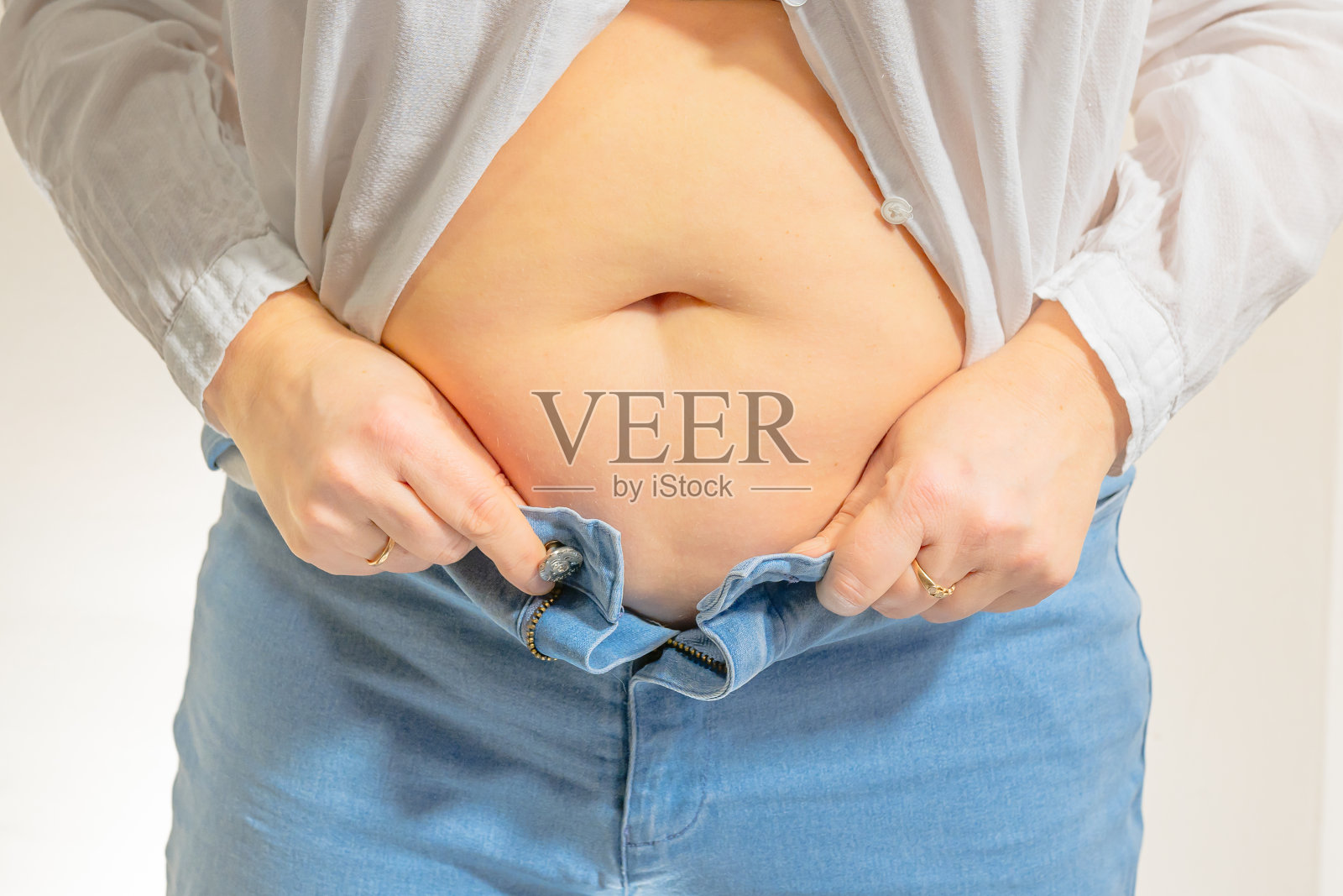 胖女人的腹部特写，裸露的肚脐，腰部没有扣纽扣的牛仔裤。照片摄影图片