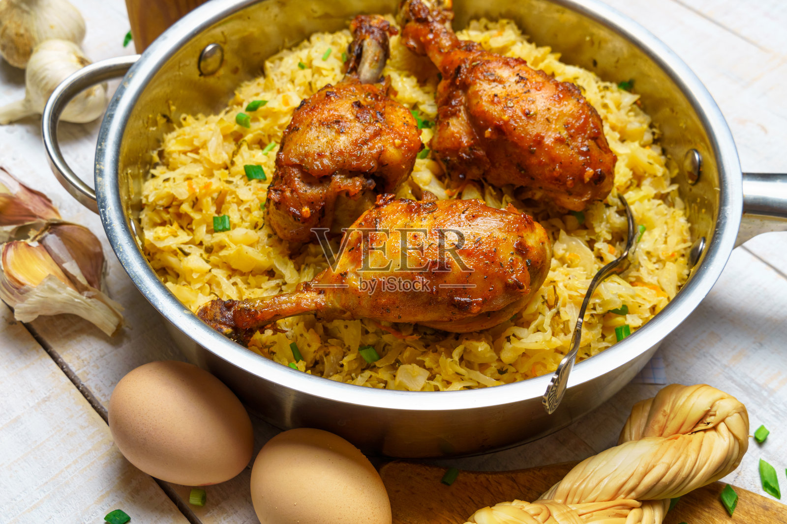 用平底锅煎鸡腿，配以炖白菜、大蒜和大葱、奶酪、鸡蛋和盐，以及生的和熟的食物，白色木板为背景，呈现出一种乡村风格照片摄影图片