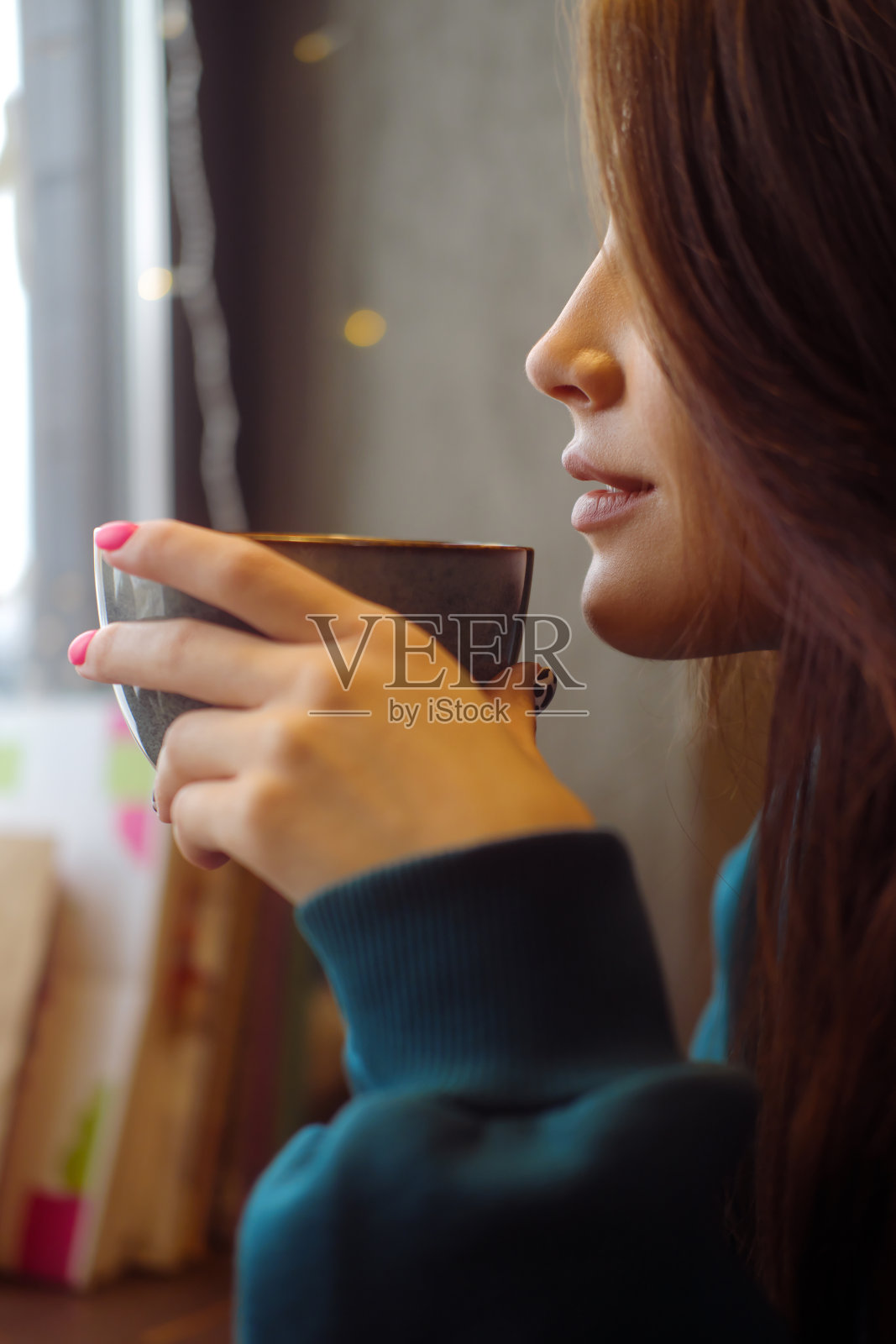 一个穿着蓝色连帽衫的漂亮女孩坐在咖啡桌旁。女人用一个大杯子喝咖啡。舒适的气氛。照片摄影图片