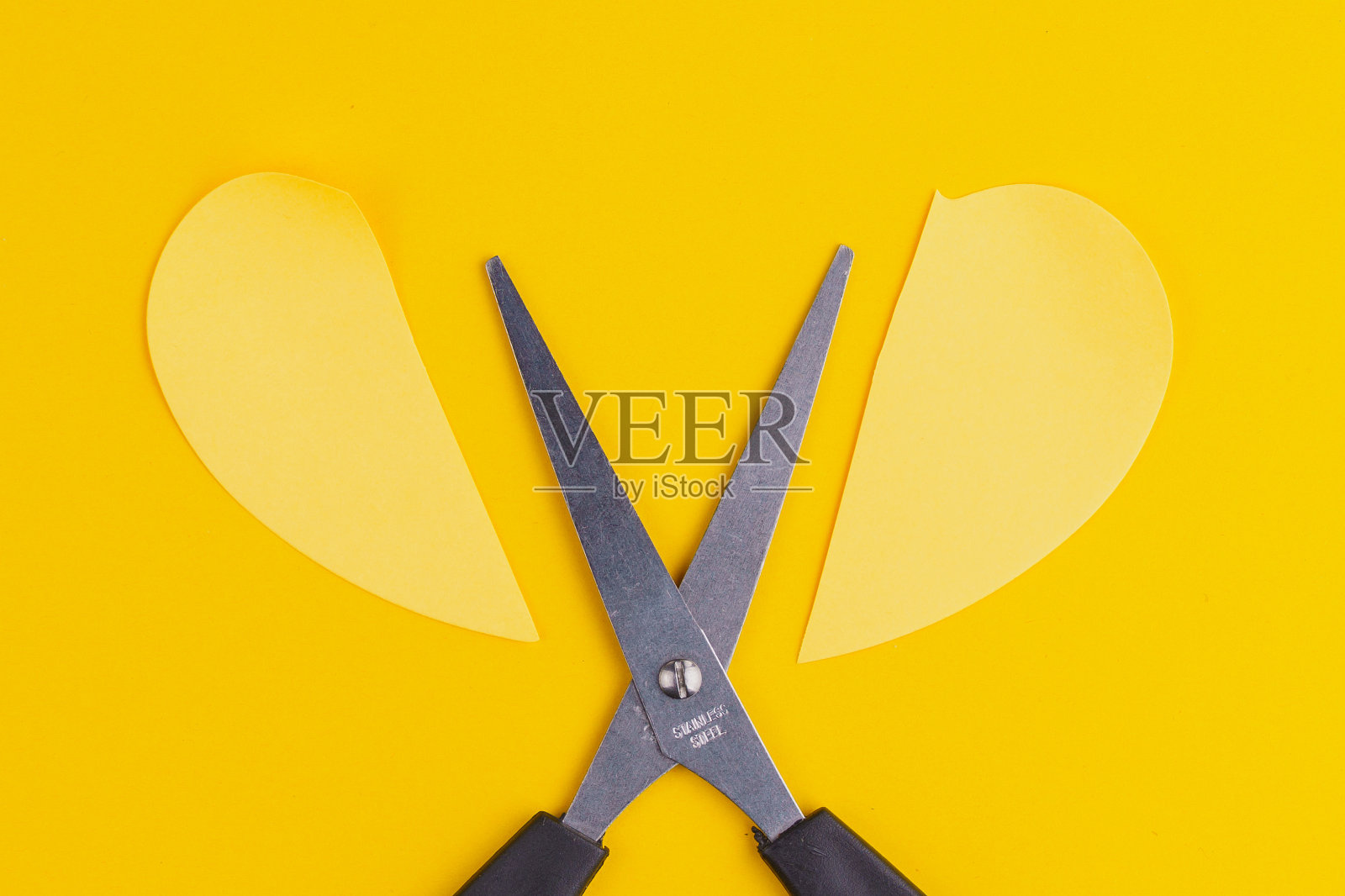 剪刀把一张纸剪成两半。关系破裂的概念。黄色背景和复制空间照片摄影图片