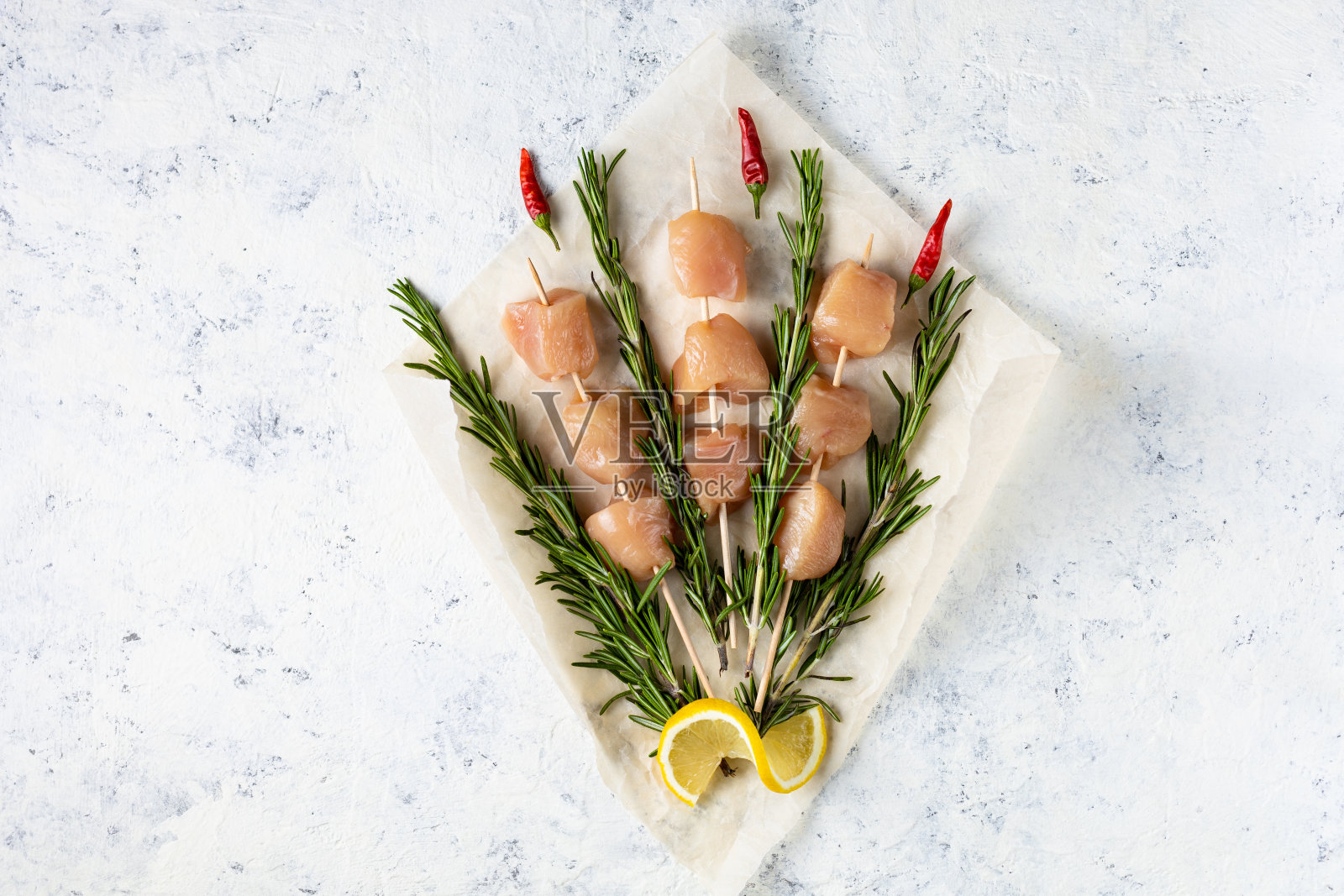 生鸡肉串和迷迭香在浅色的背景上形成一束花。照片摄影图片