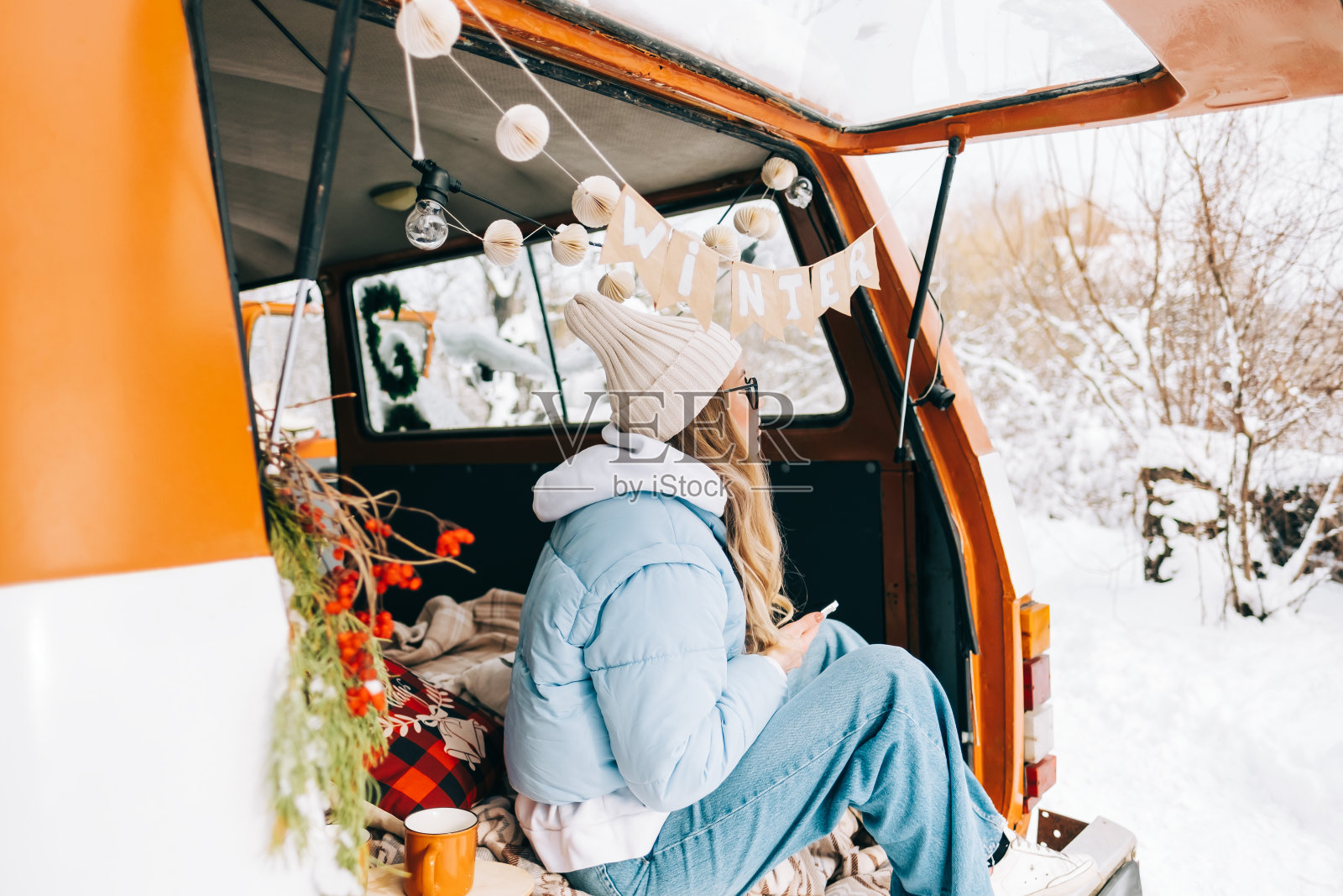 年轻的白人妇女坐在一辆车在冬天的一天，在一辆面包车旅行和享受假期。照片摄影图片