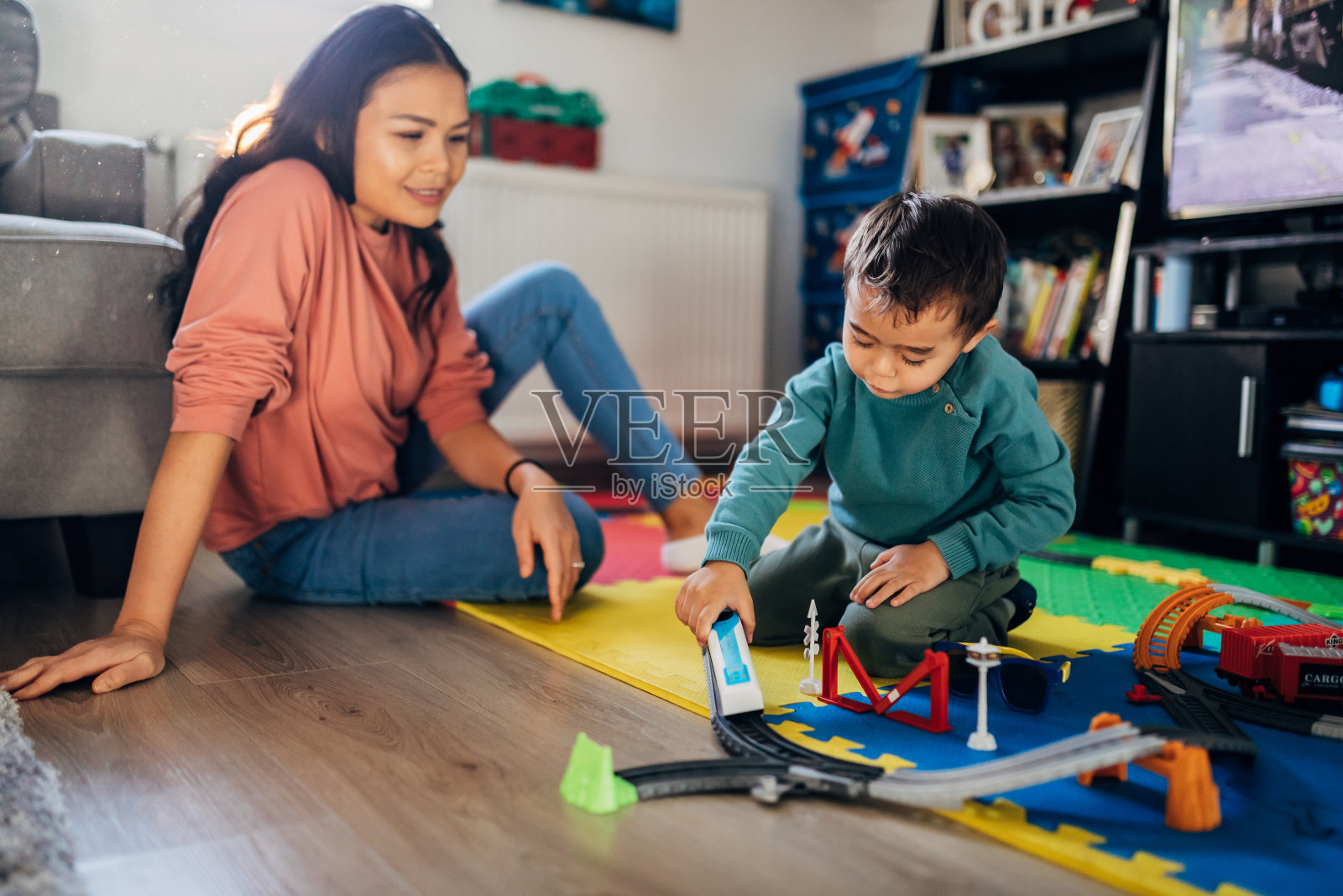一位微笑的母亲坐在她三岁的儿子旁边，玩着他最喜欢的玩具——火车。照片摄影图片