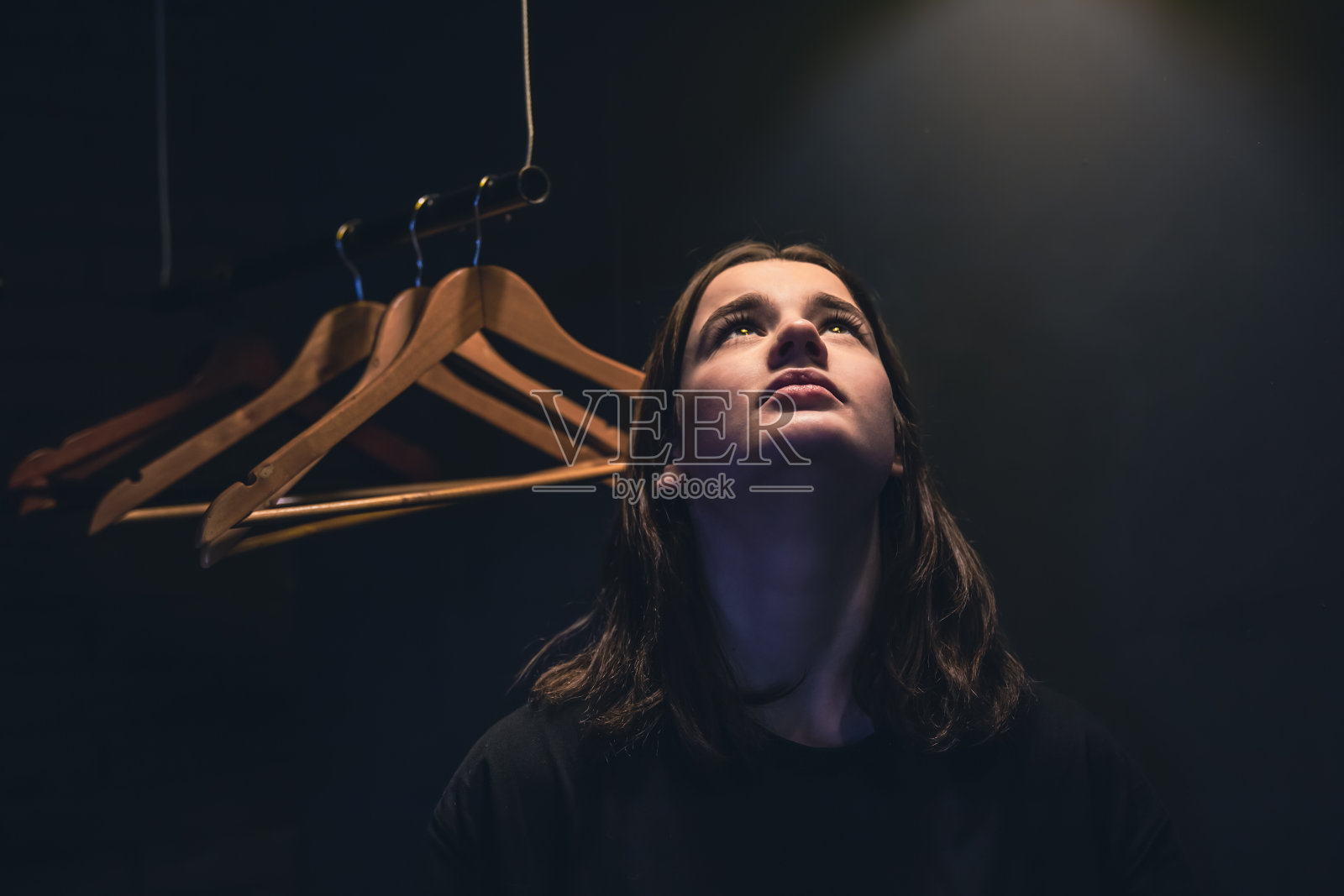 年轻女子在黑暗的灯光下，站在空荡荡的衣架旁照片摄影图片