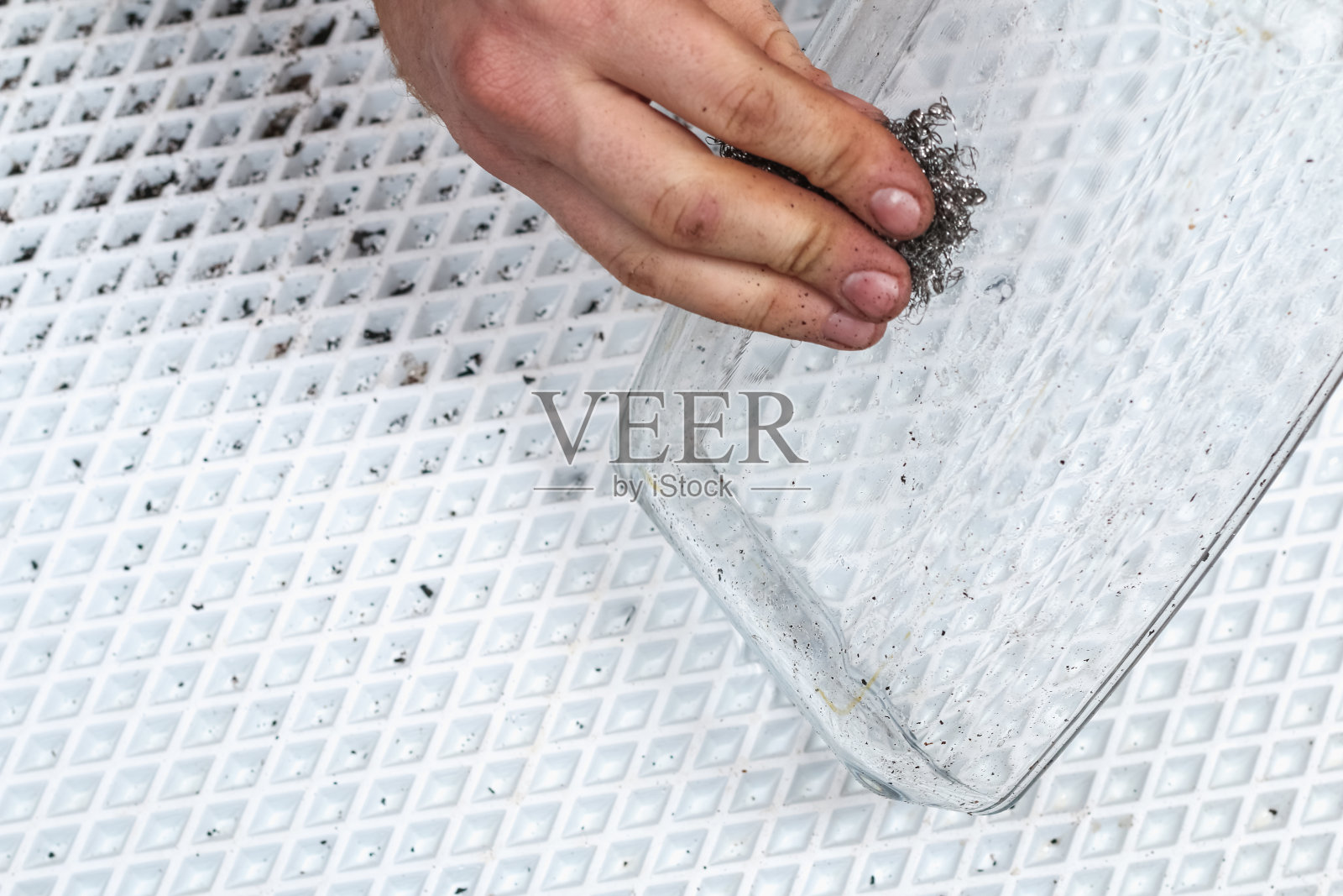 一名男子正在用铁质毛巾清洗沾满一层厚厚的碳的脏烤盘。用烟灰、、陈干油脂烘烤用的玻璃器皿。照片摄影图片