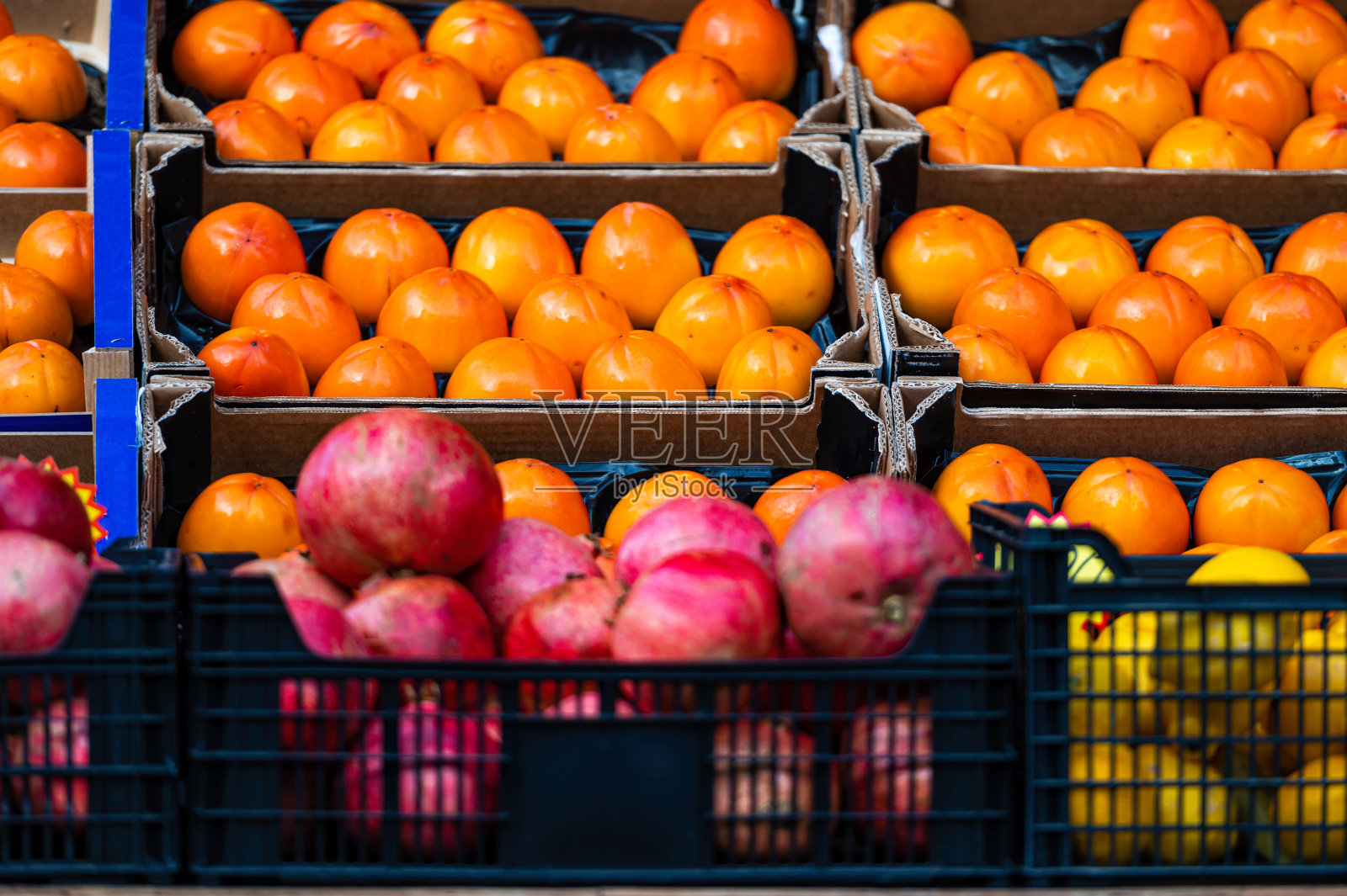 市场上一排排装在木箱里的成熟柿子、石榴和柠檬照片摄影图片