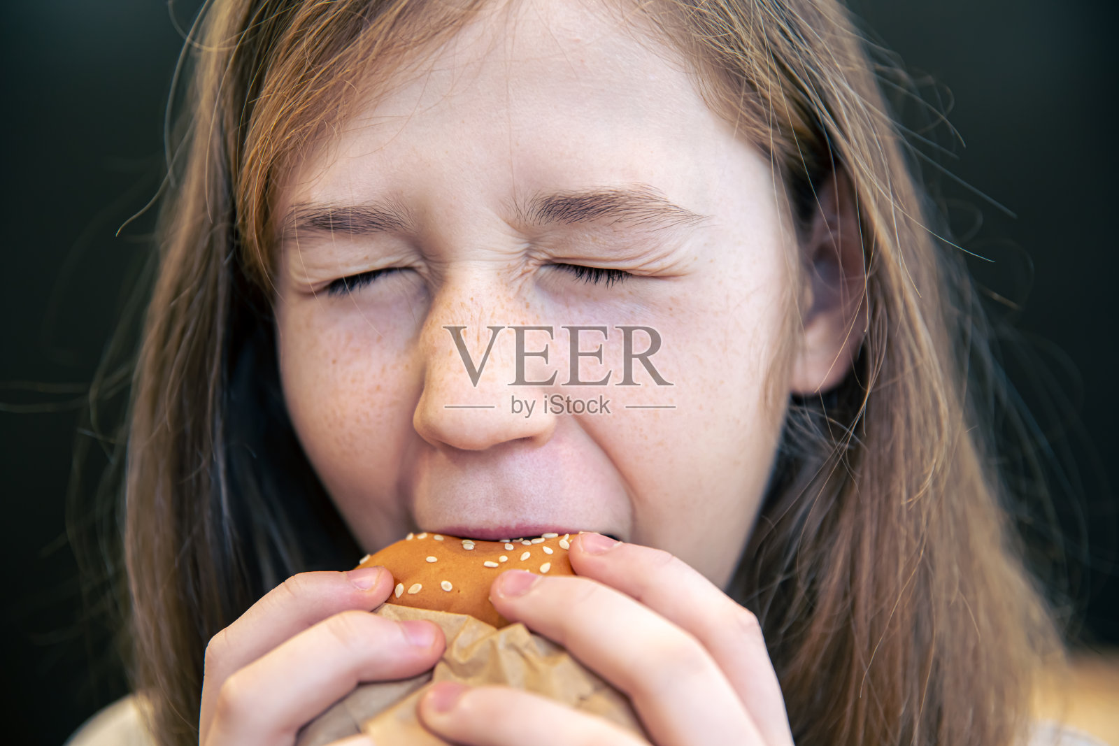 一个长着雀斑的小女孩在吃汉堡。照片摄影图片