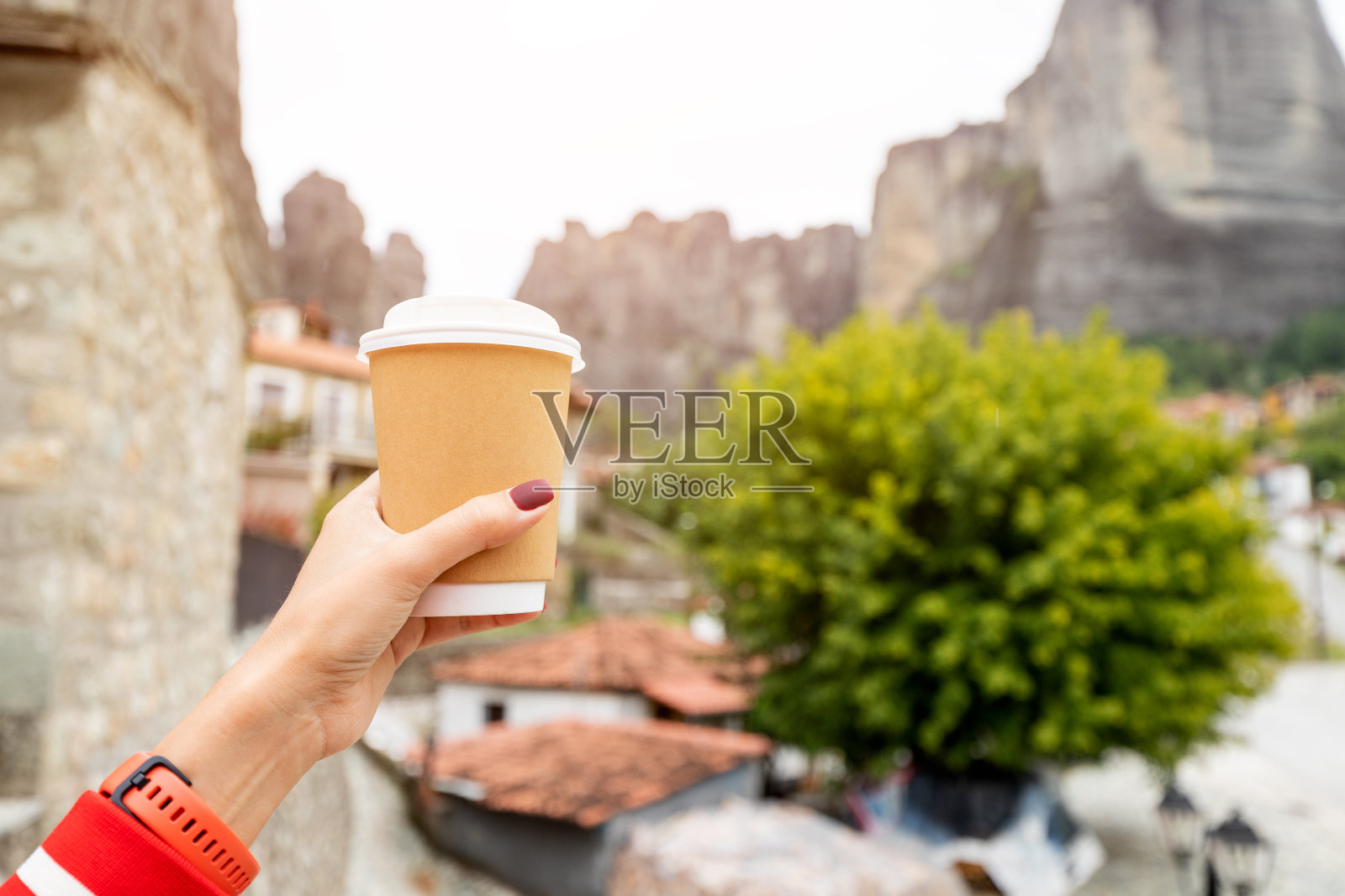 手拿一个带着新鲜热咖啡或茶的外卖纸杯，背景是著名的迈泰奥拉山脉照片摄影图片