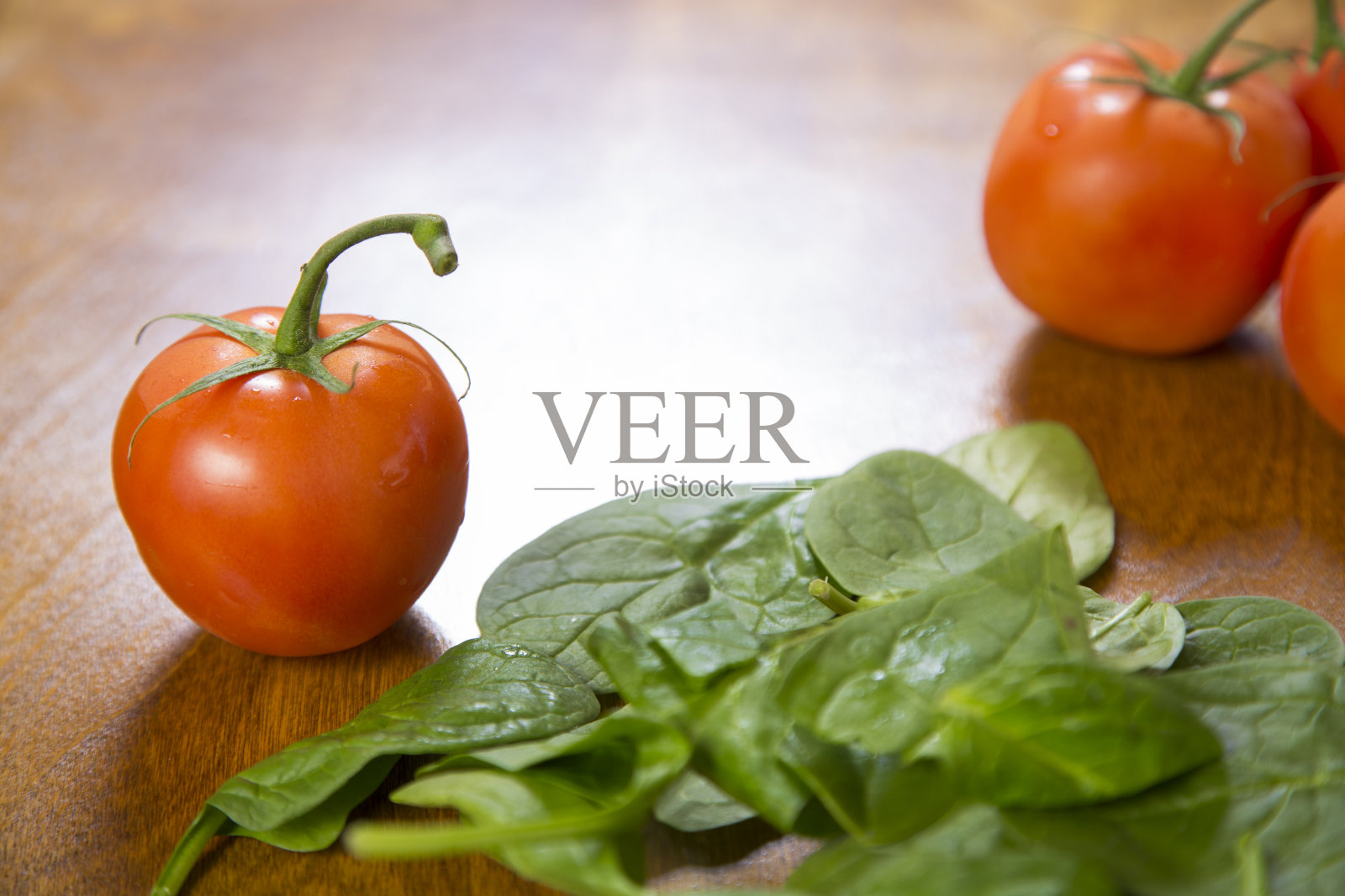 一串新鲜成熟的西红柿和一盘嫩菠菜。木制的桌子。副本的空间。素食食物。照片摄影图片