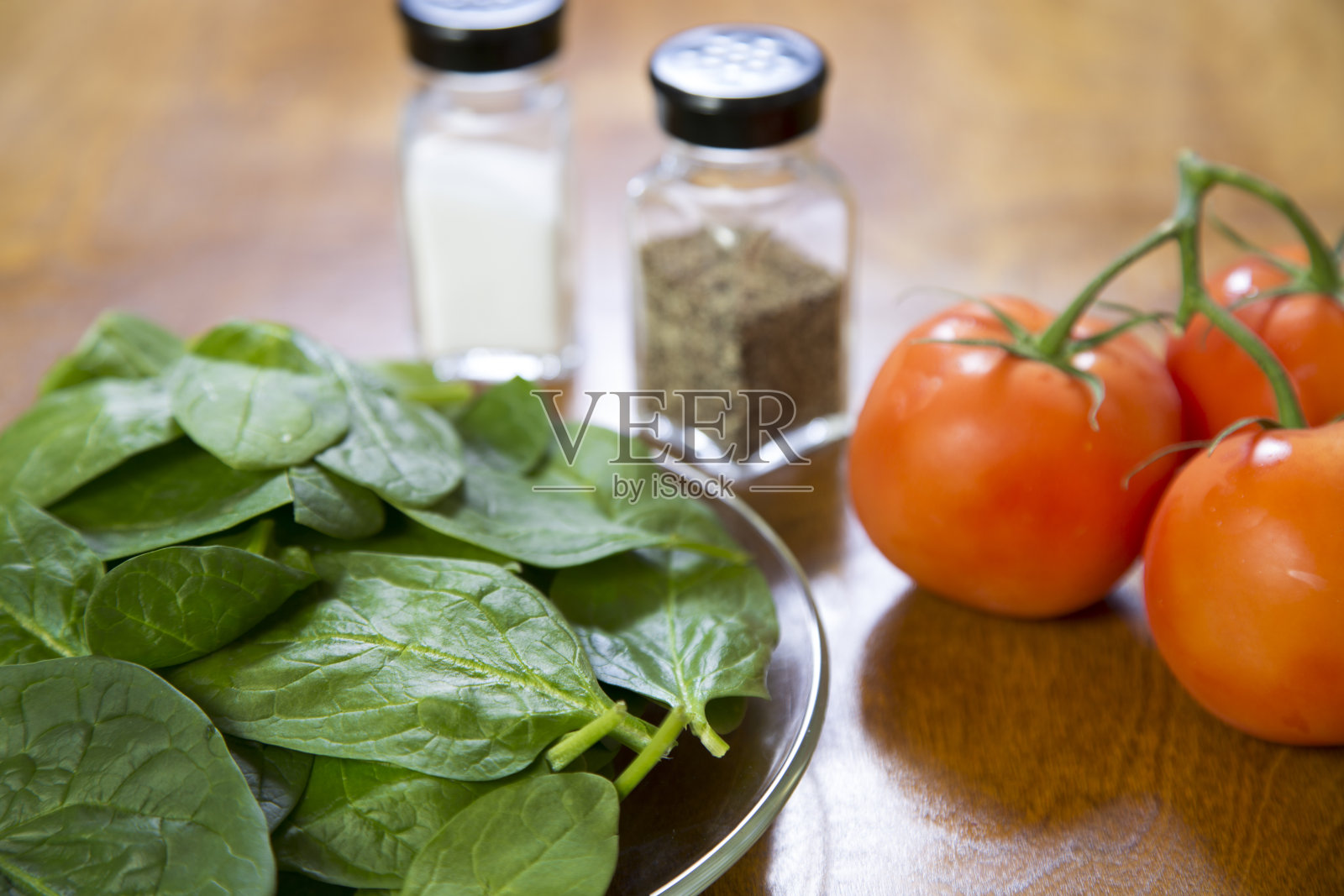 一串新鲜成熟的西红柿和一盘嫩菠菜。木制的桌子。盐和胡椒瓶。副本的空间。素食食物。照片摄影图片