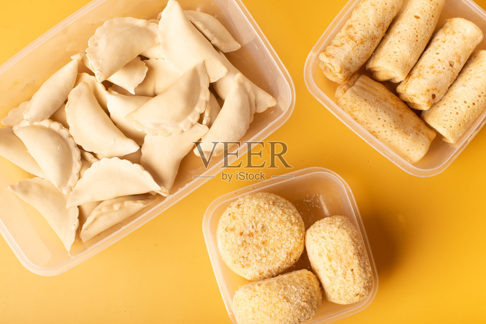 煎饼、饺子和肉排装在黄色背景的容器里。冷冻半成品照片摄影图片