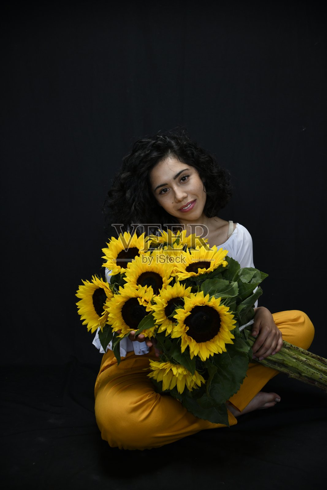 年轻的春天女人拥抱向日葵与黑暗的背景照片摄影图片