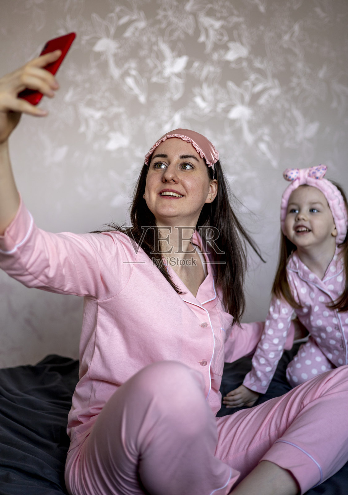 快乐的母女穿着睡衣，在床上用智能手机自拍照片摄影图片