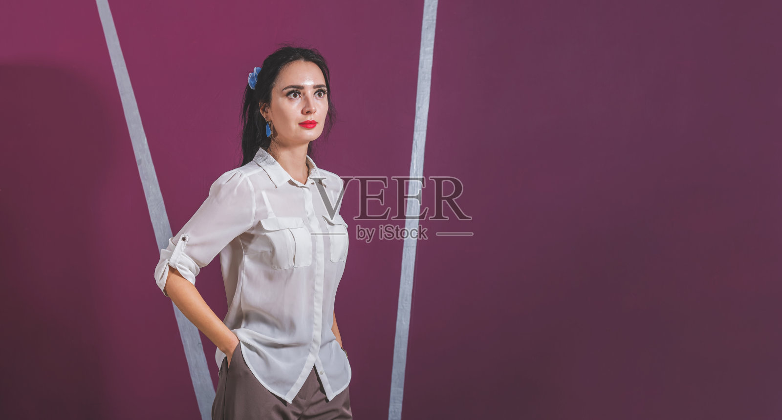 穿着白衬衫的漂亮女商人站在办公室里，靠着粉红色的墙。视线远离摄像机。照片摄影图片