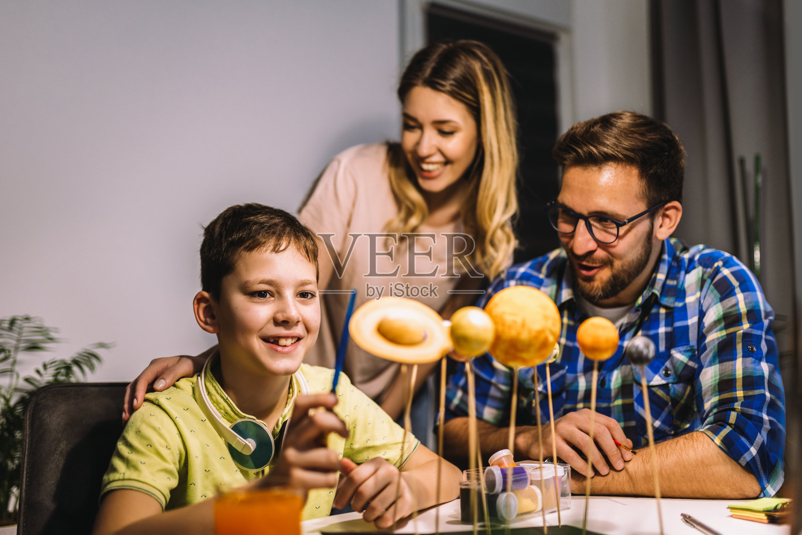 快乐的学校男孩和他的父母在家里为学校的科学项目做一个太阳系照片摄影图片