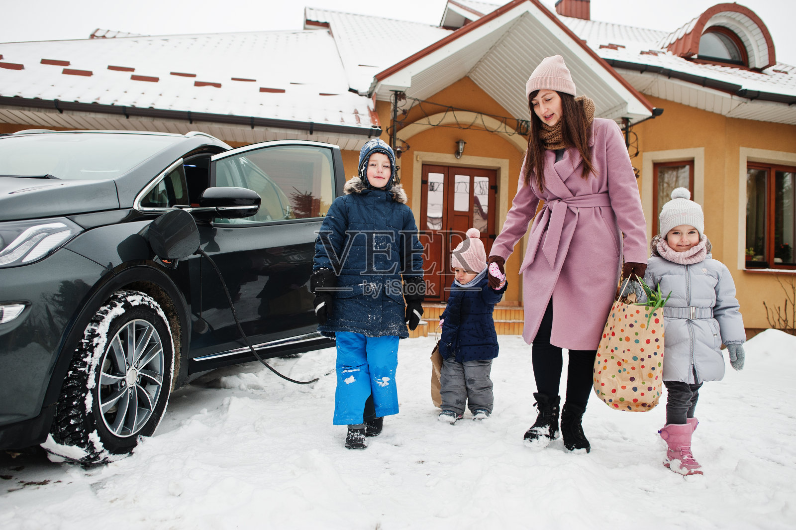 一个带着孩子的年轻女子在自家院子里拿着环保袋给电动汽车充电。照片摄影图片