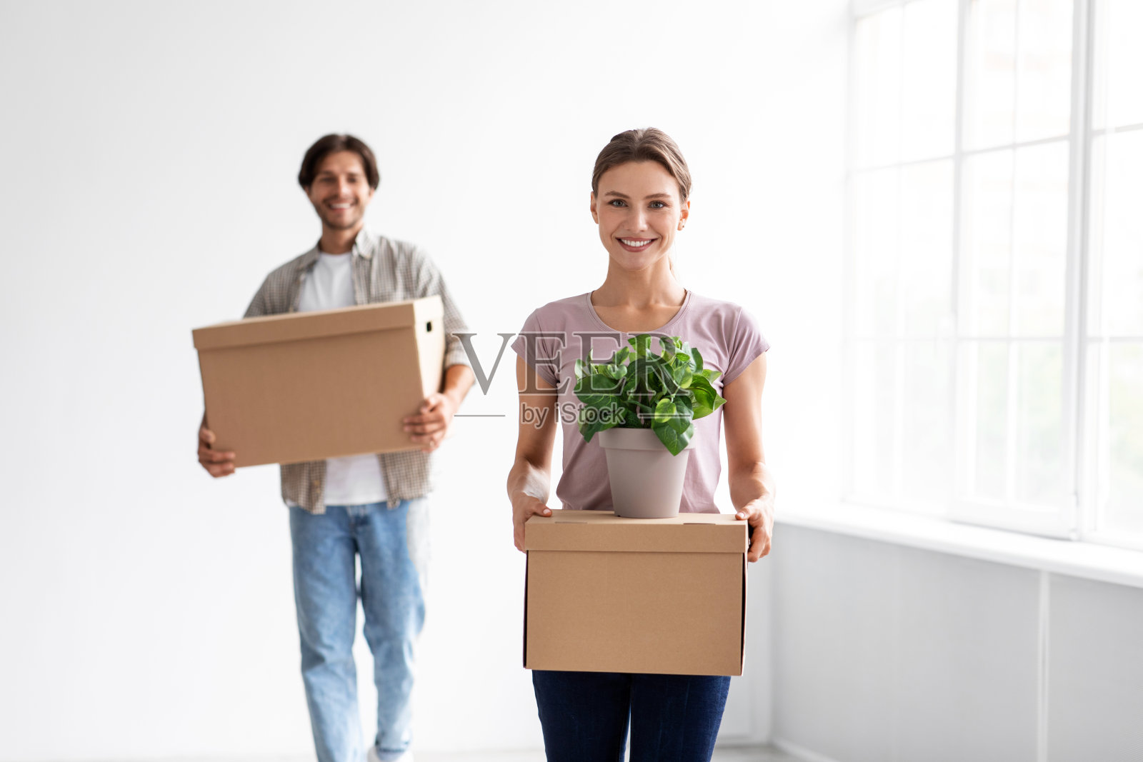 满足了欧洲千禧一代的家庭在随意携带的纸板箱与财产和花盆在空房间照片摄影图片